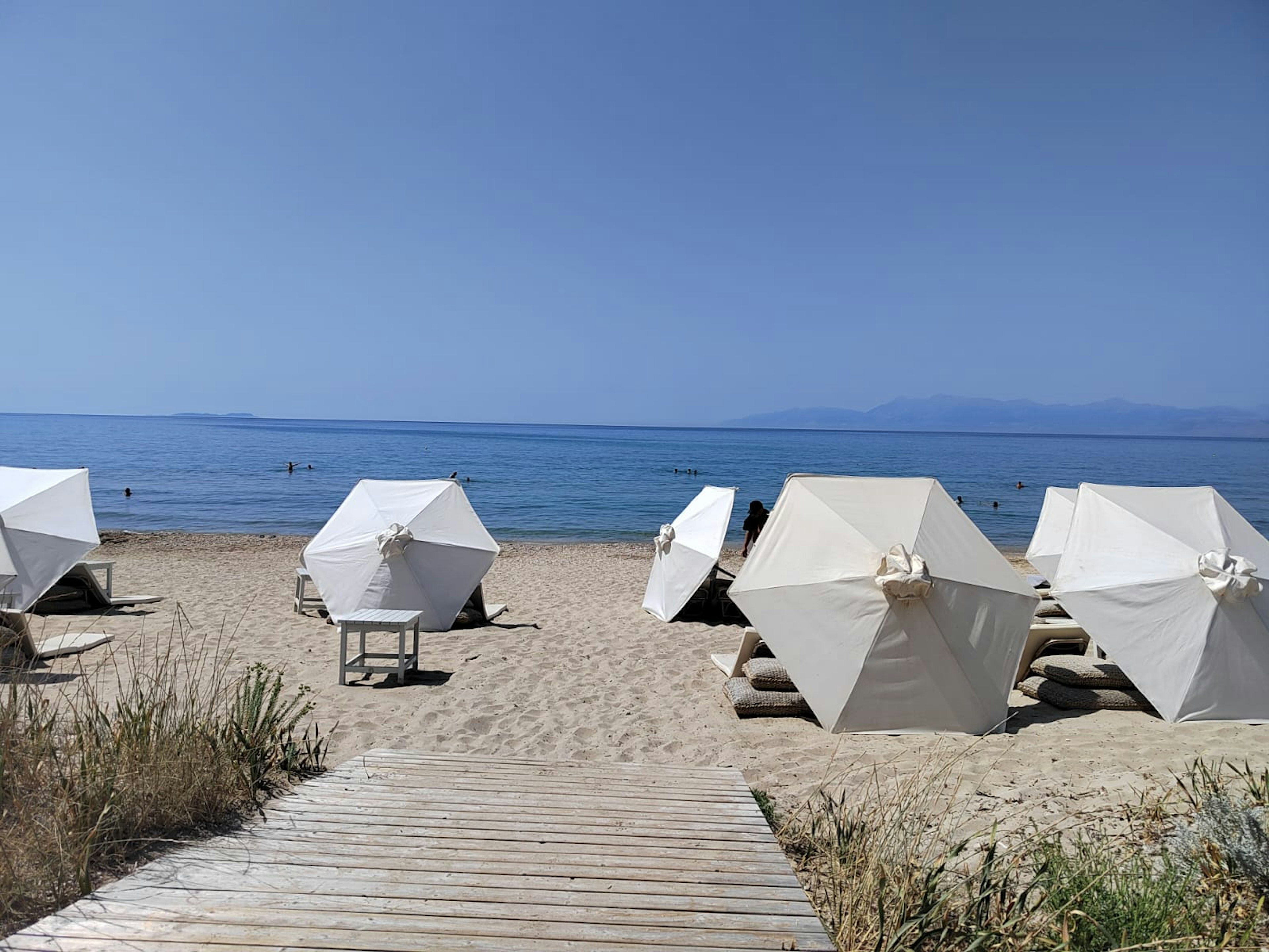 Strandszene mit weißen Sonnenschirmen und blauem Ozean