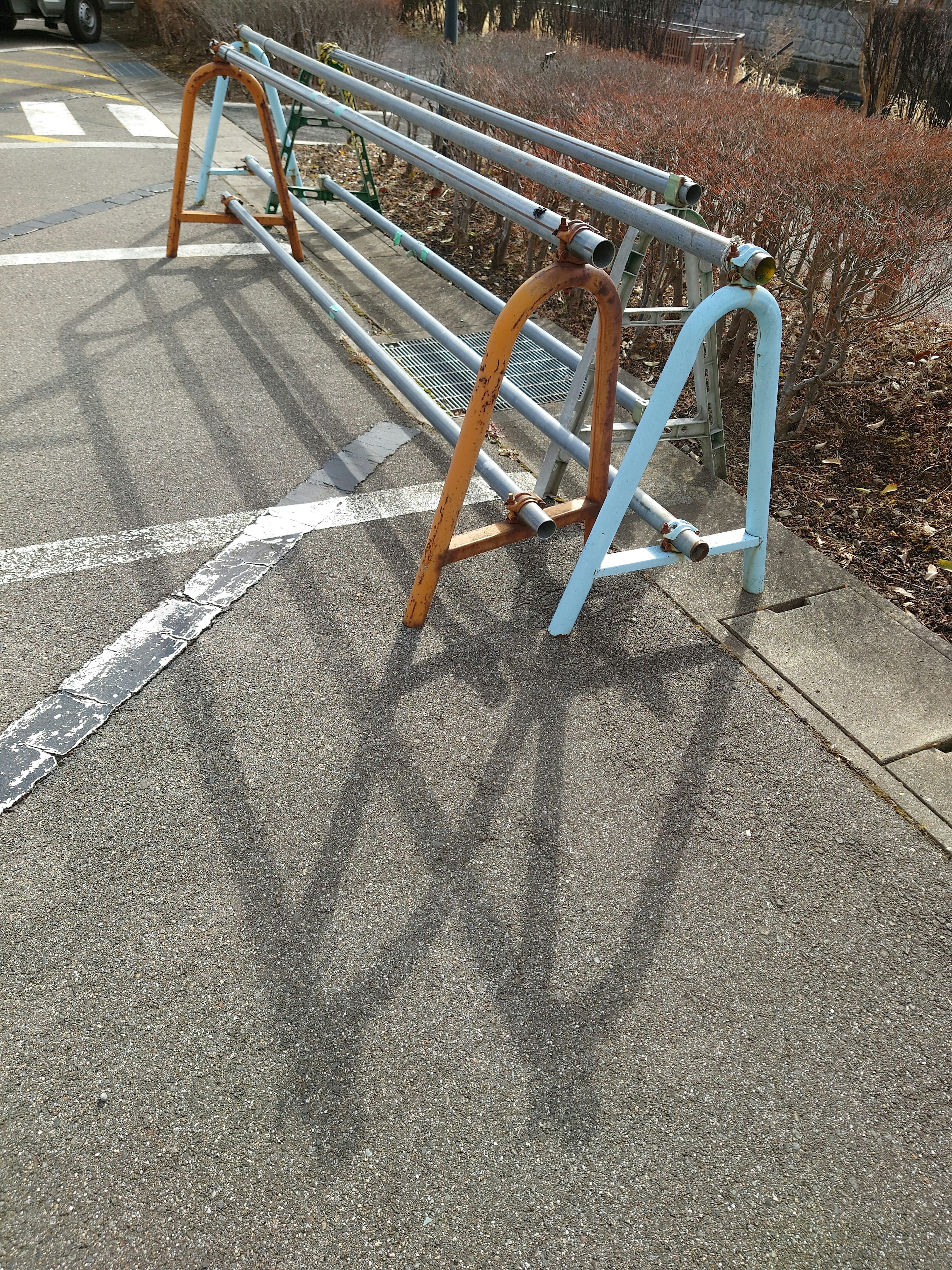 Soporte para bicicletas de metal en colores azul y naranja proyectando sombras en el pavimento