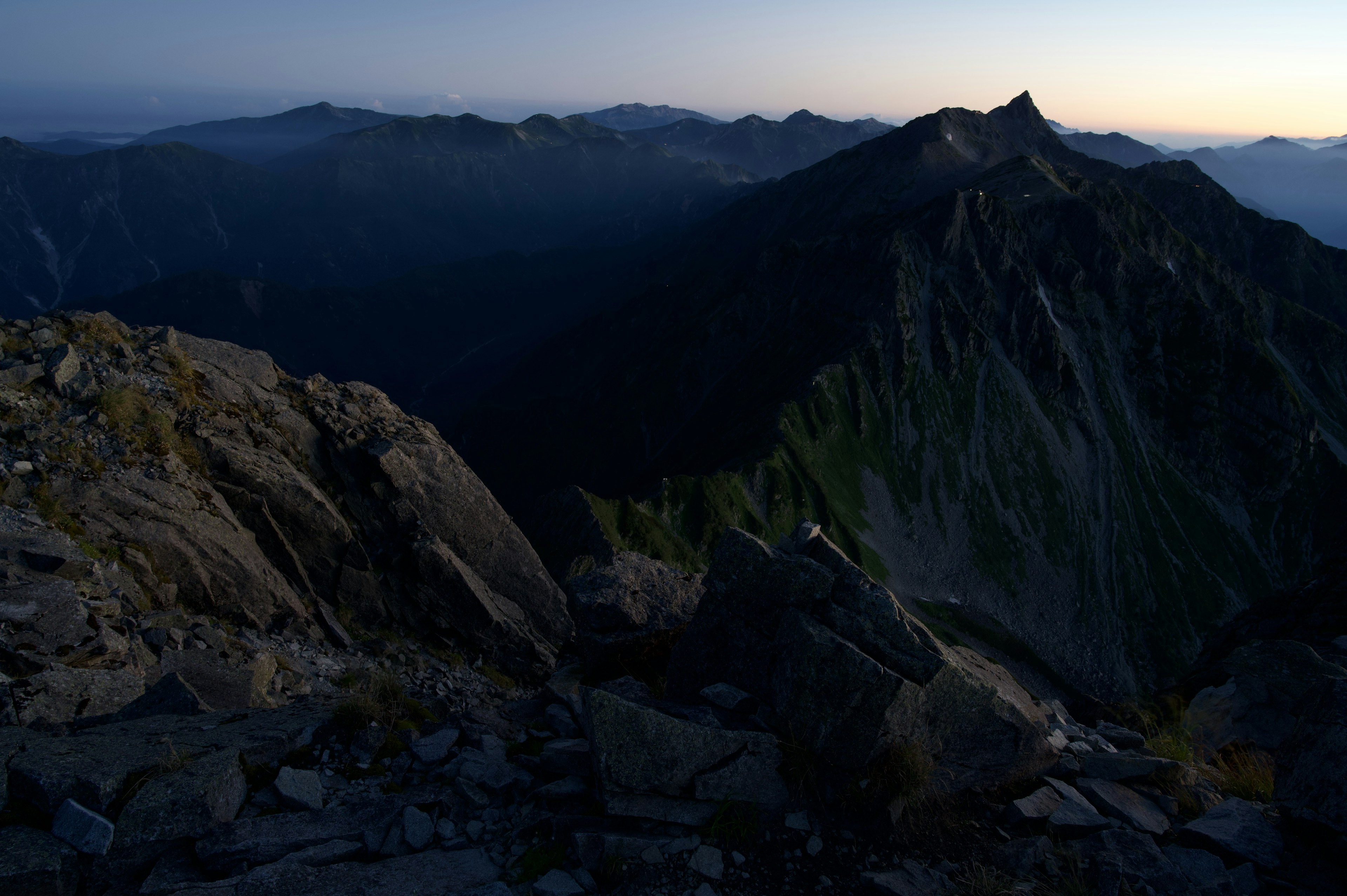 Paysage de l'aube depuis un sommet de montagne avec des crêtes ombragées et un premier plan rocheux