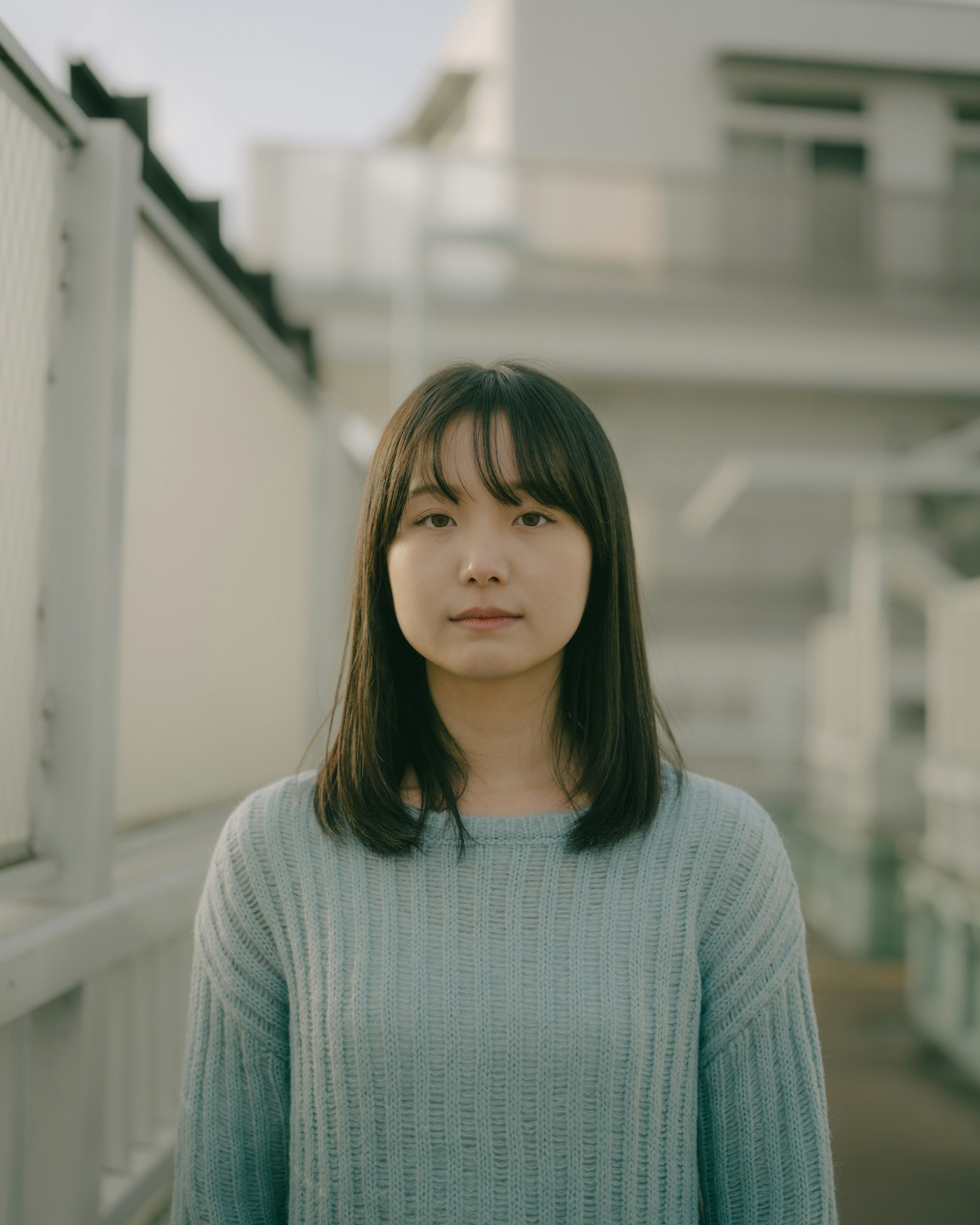 Une femme portant un pull bleu clair se tenant avec une expression calme devant un bâtiment