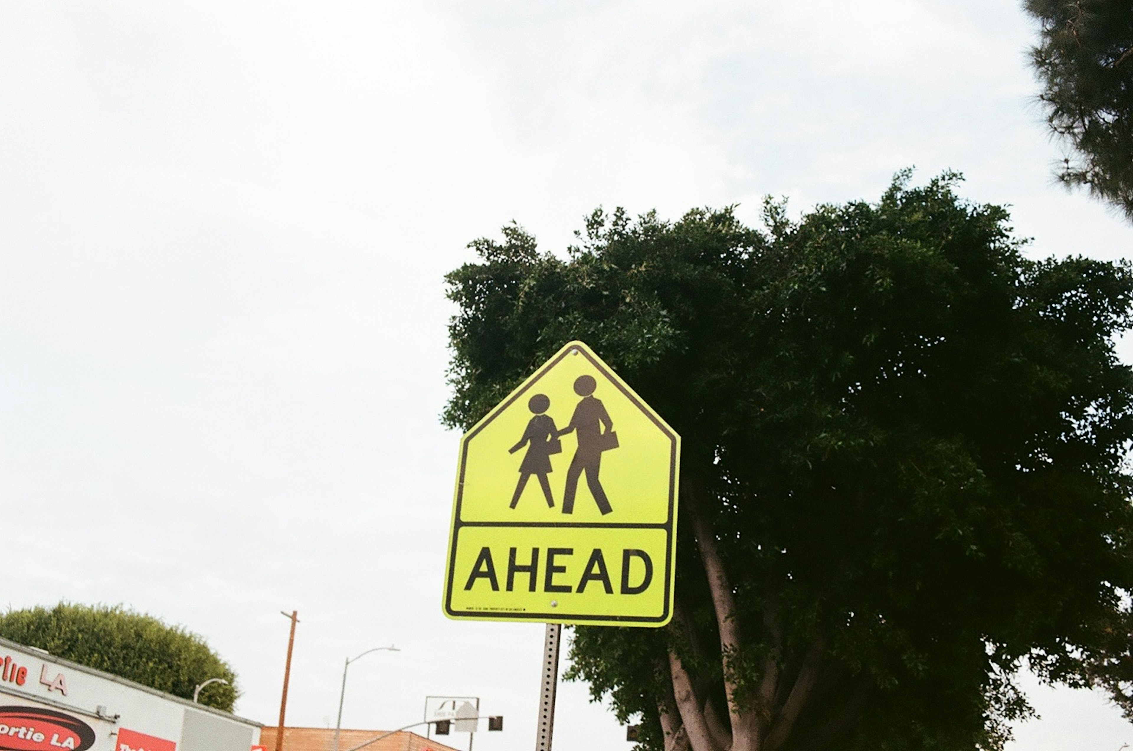 Gelbes Fußgängerwarnschild mit dem Wort AHEAD und zwei Figuren