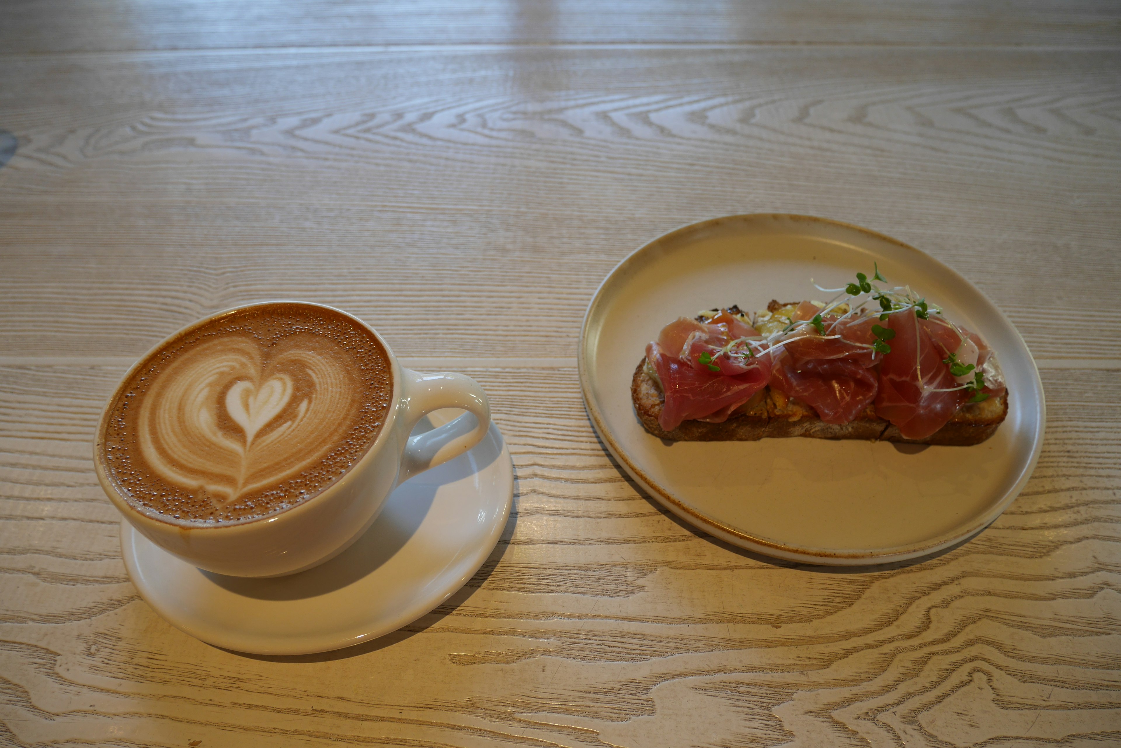 Una tazza di latte con arte a forma di cuore e un piatto di toast guarnito con carne e erbe