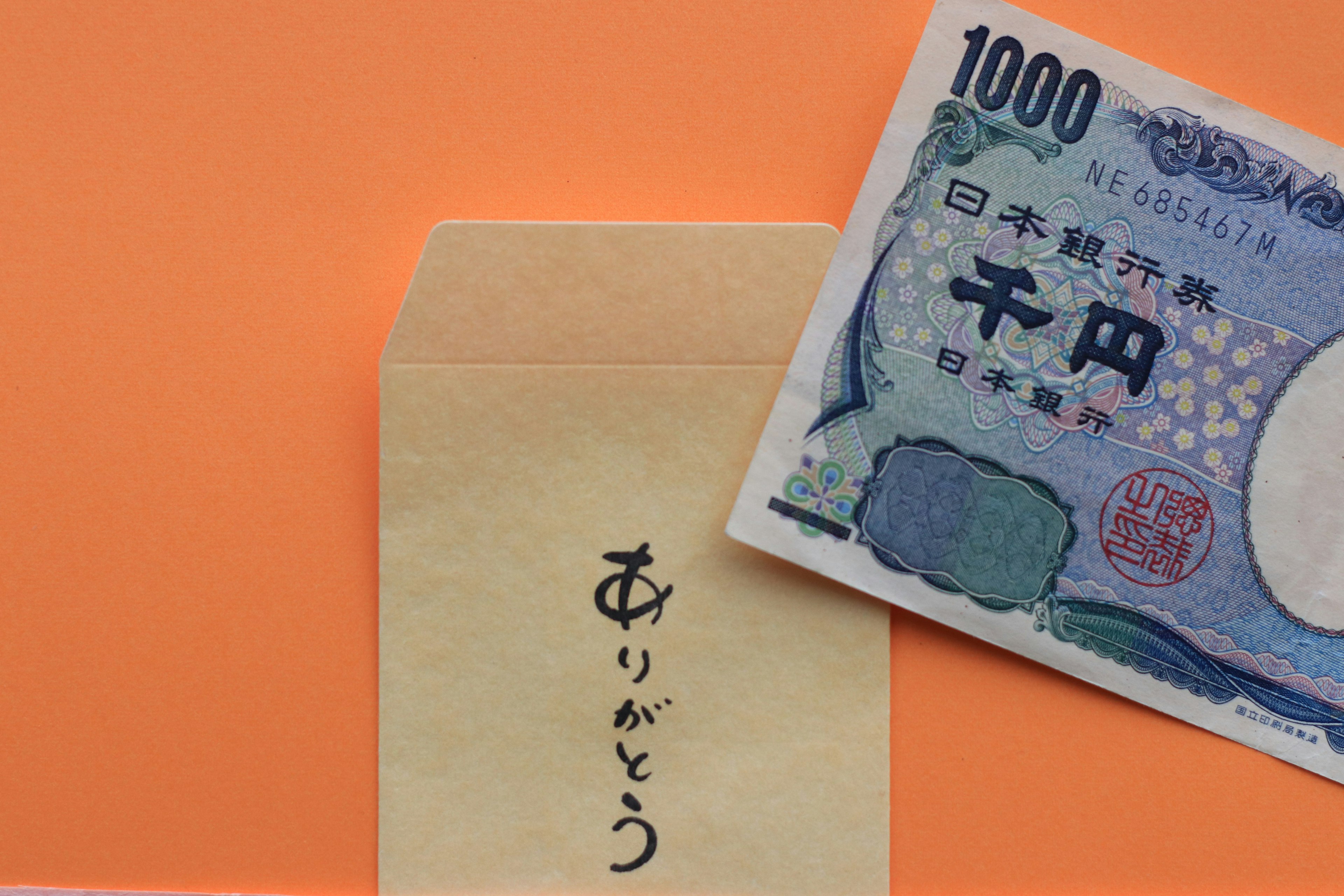 A thousand yen bill next to an envelope with thank you written on it against an orange background