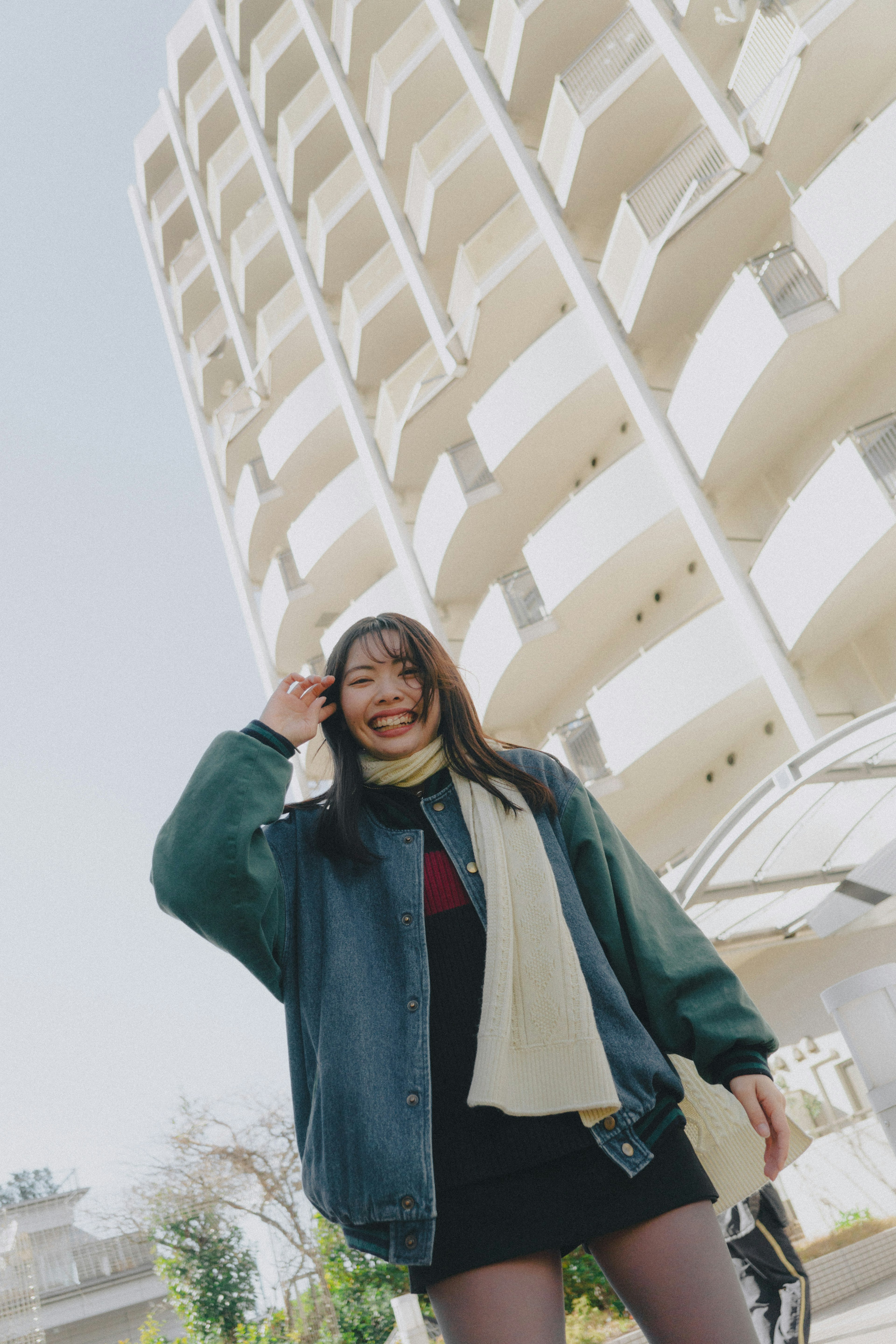 Mujer sonriente con chaqueta verde de pie al aire libre con un edificio alto de fondo