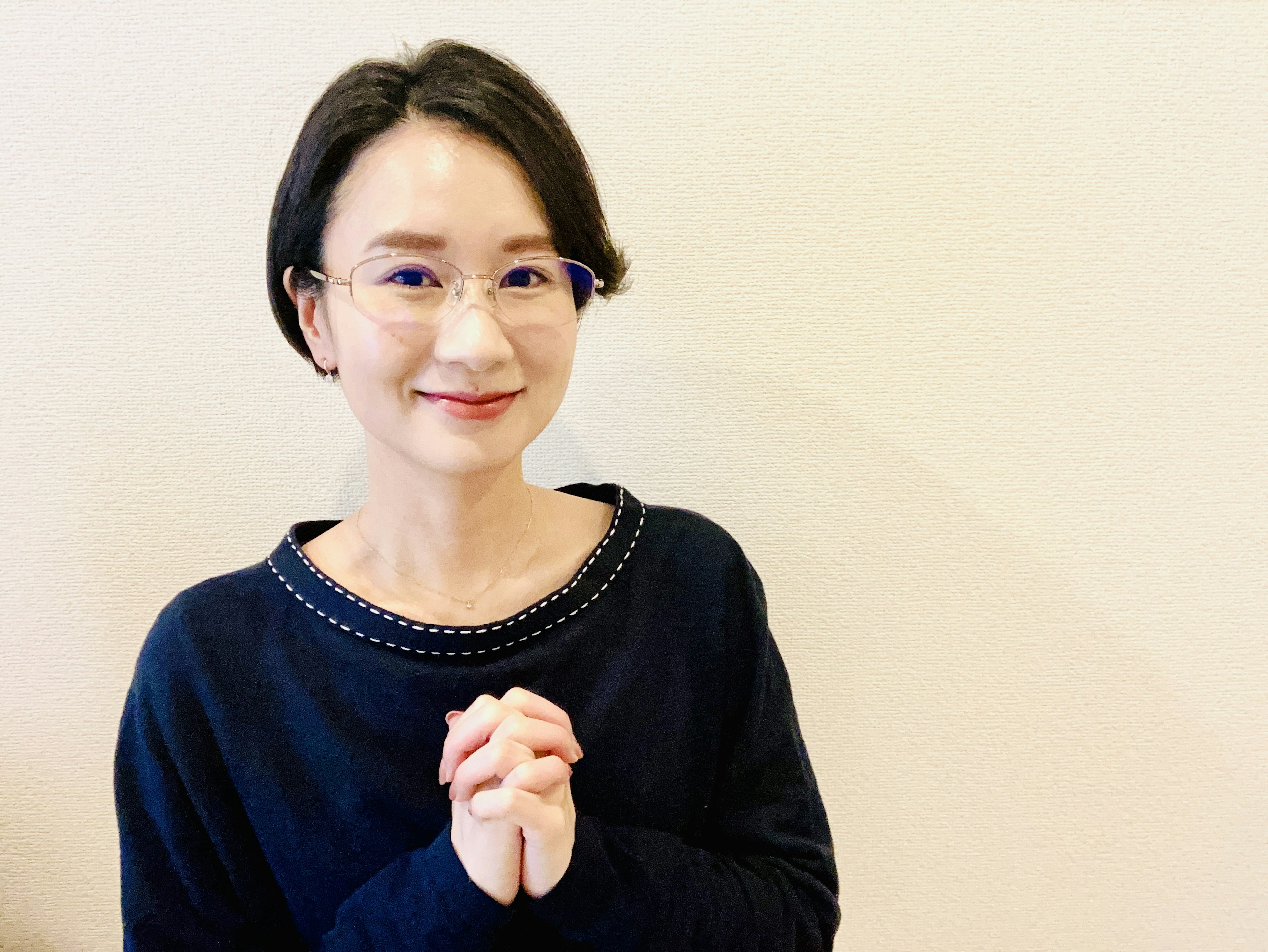 A woman in a black sweater smiling with hands clasped