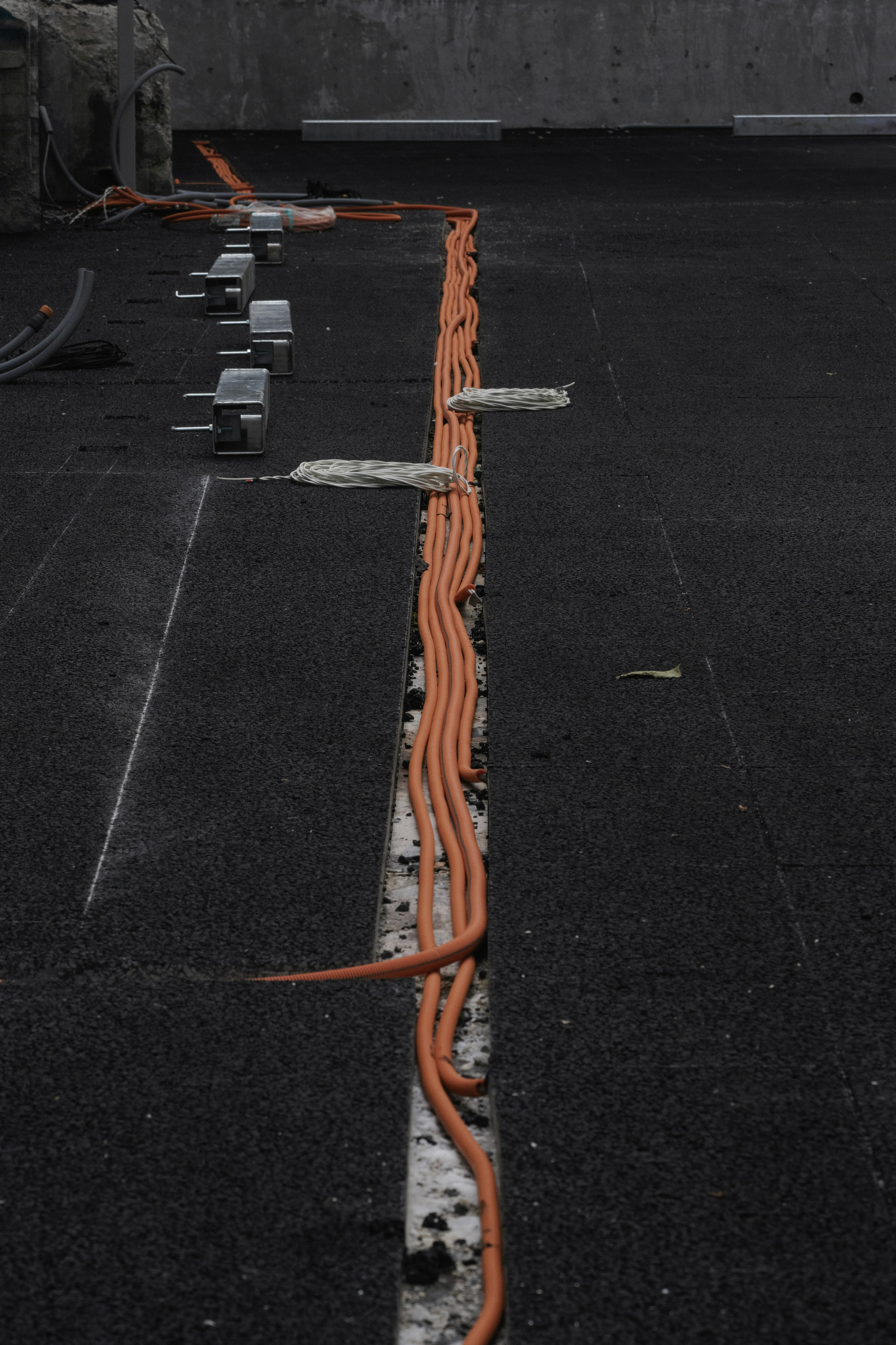 Orange cables laid out on black pavement with metal fixtures