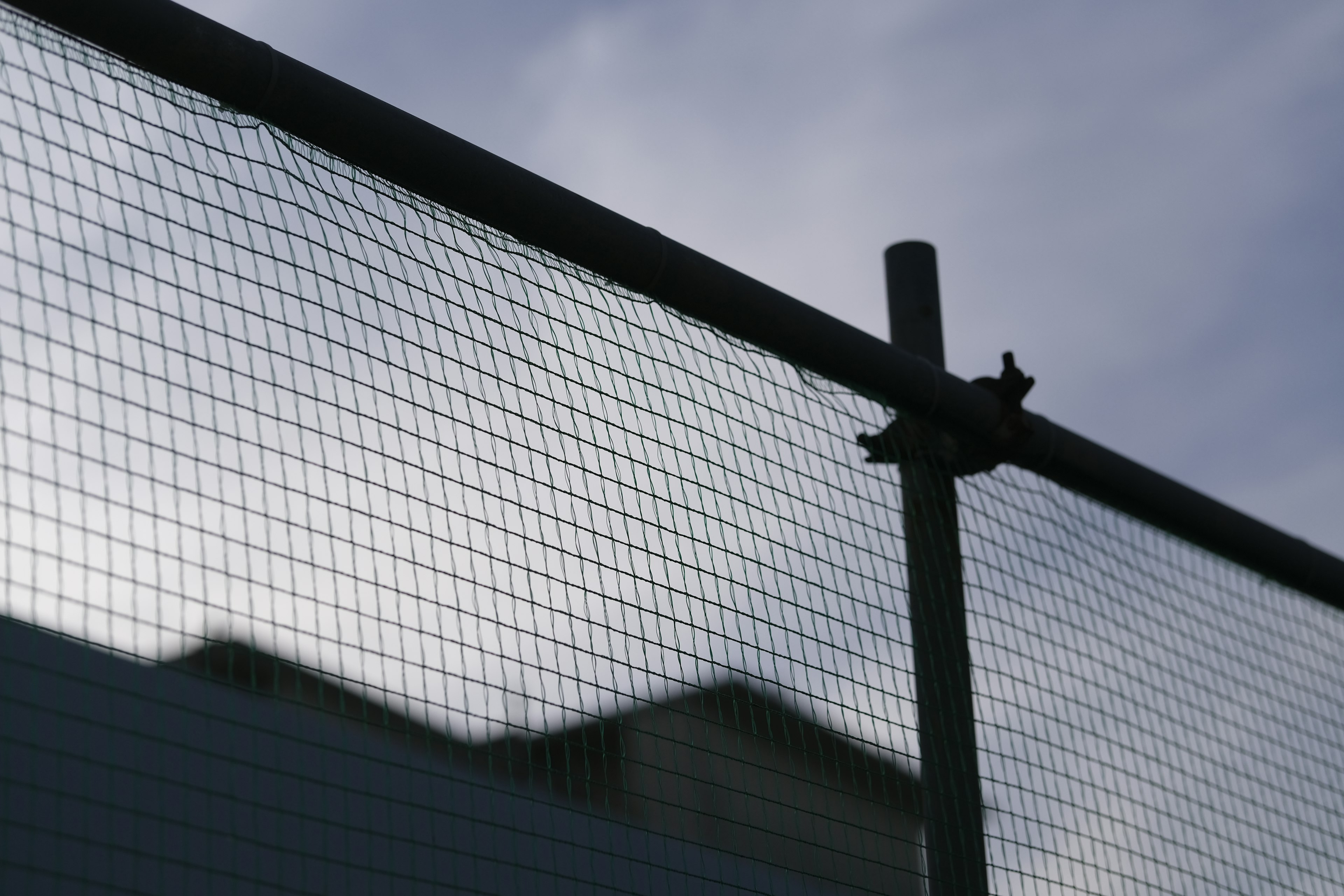 Image of a section of a metal fence with a cloudy sky in the background