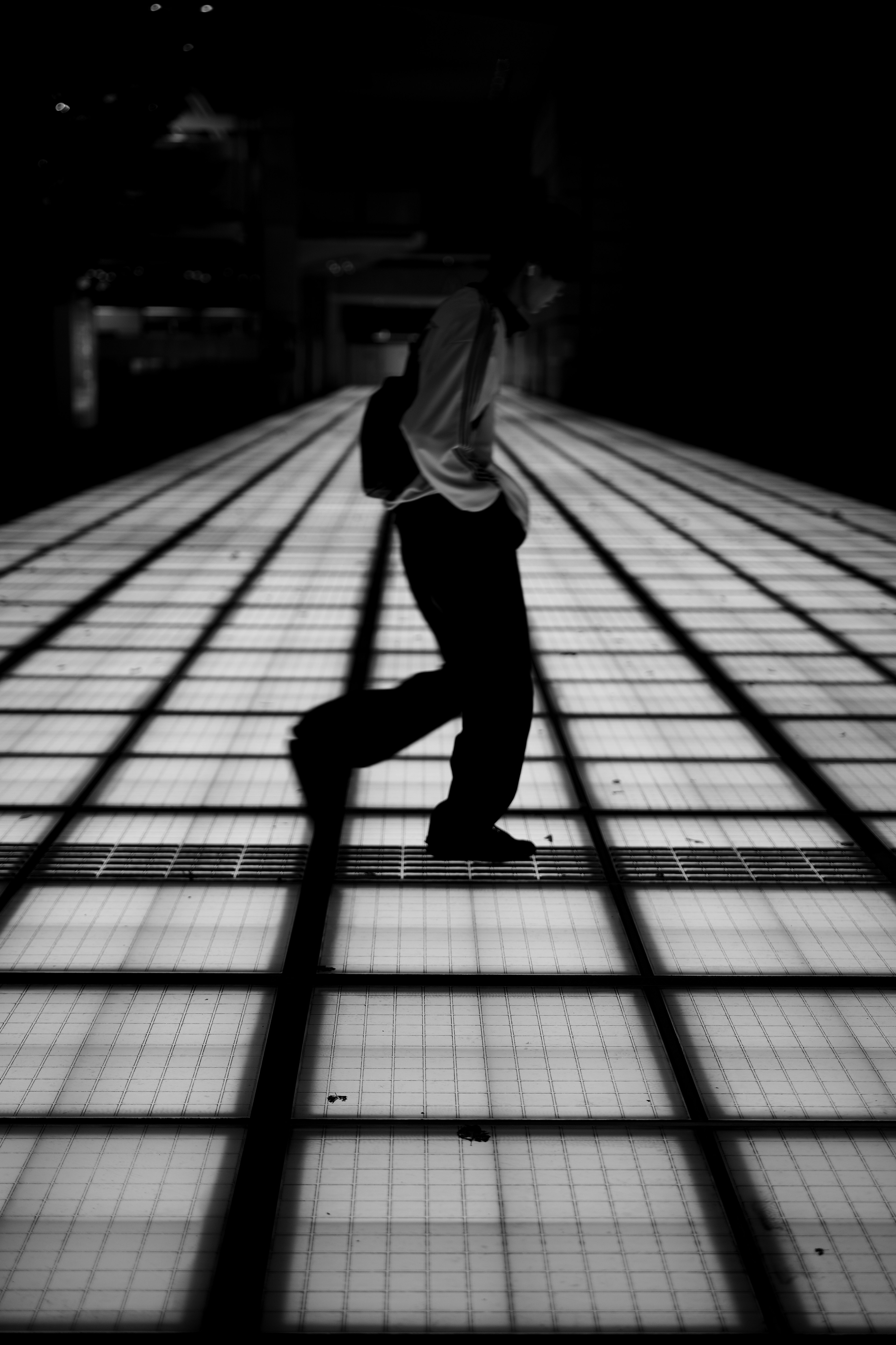 Silhouette of a person walking on a well-lit floor in black and white