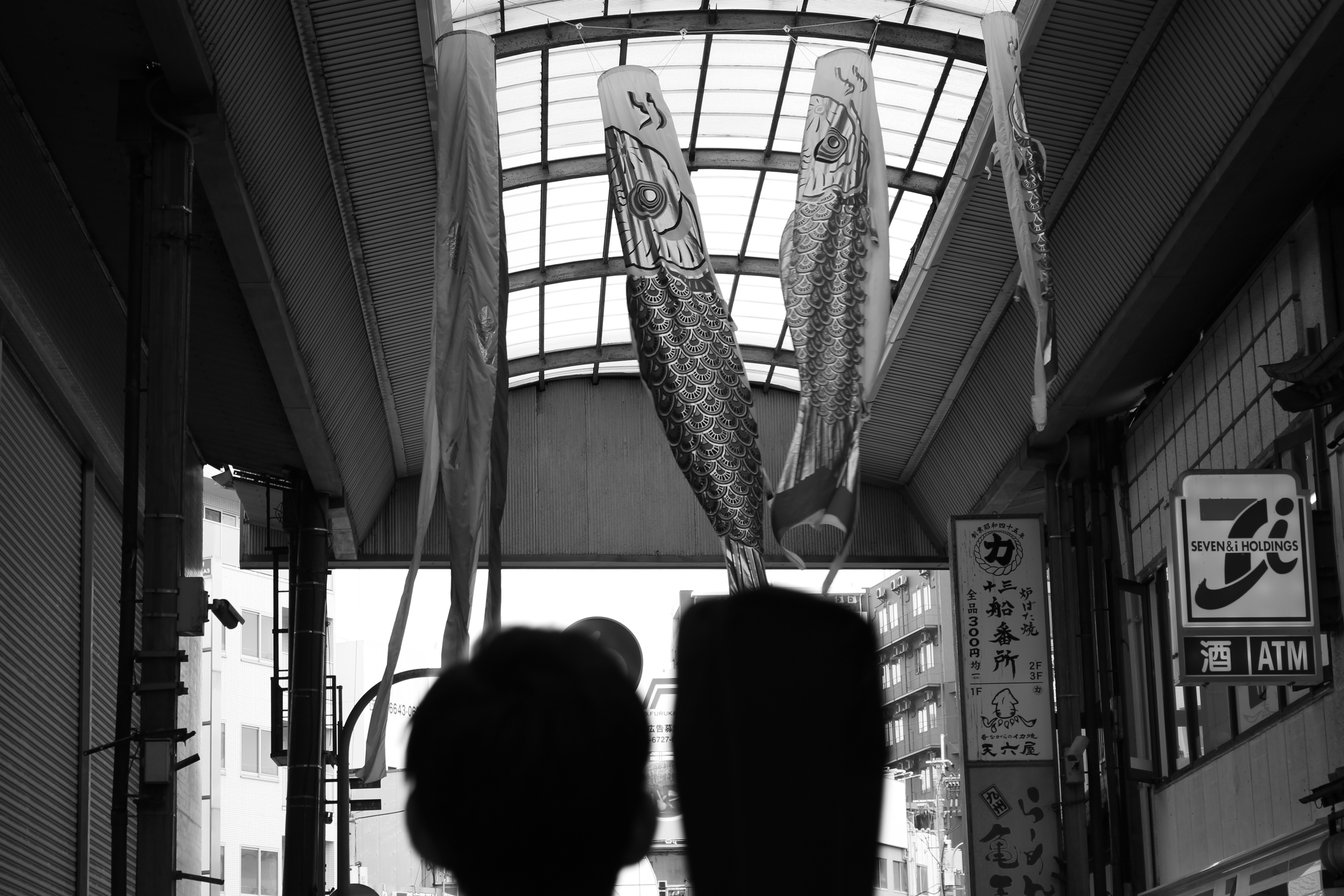 Two figures in black and white under a roof with flowing koi flags