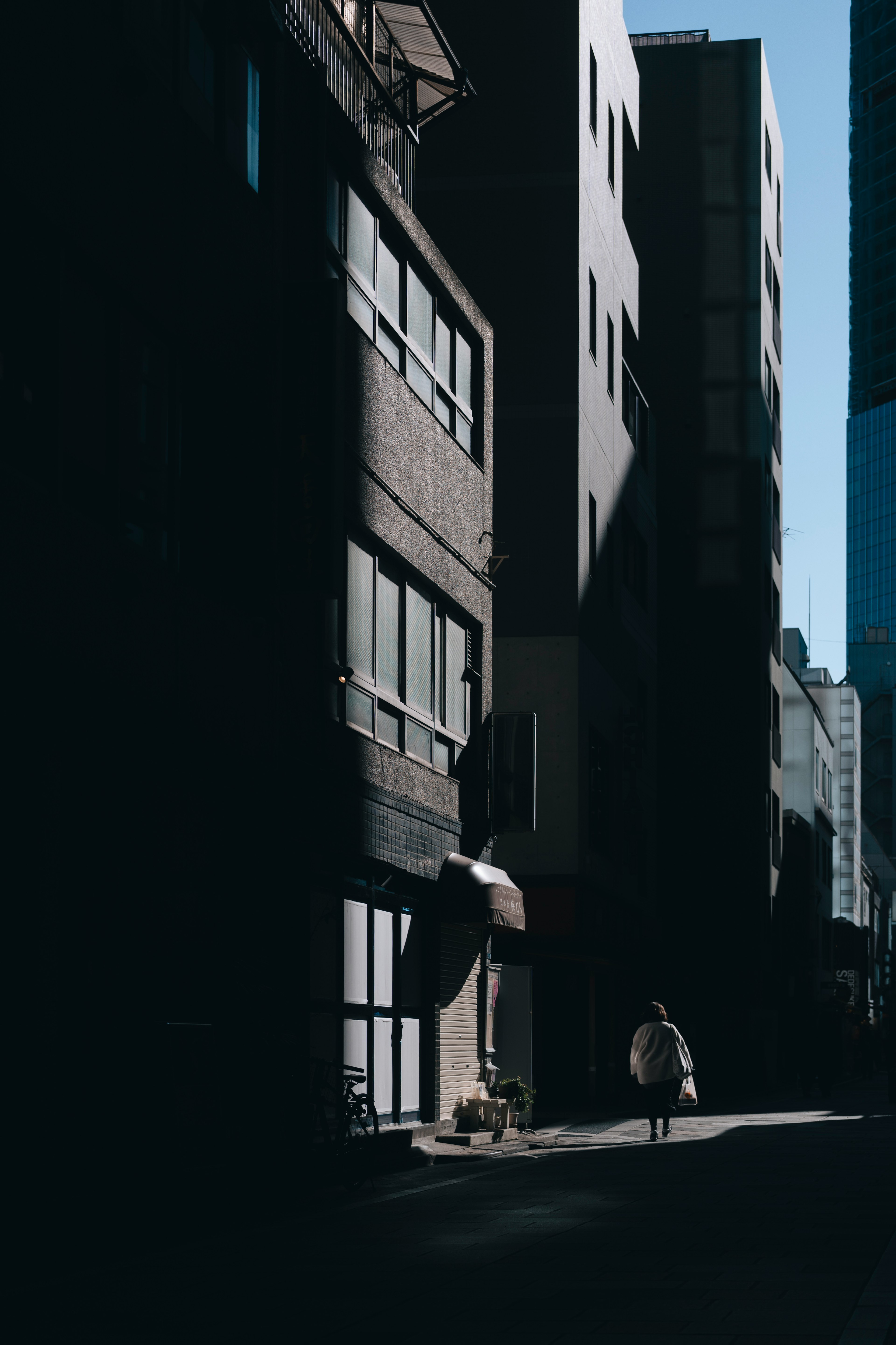 Silhouette of a person standing on a dark street with shadows of tall buildings