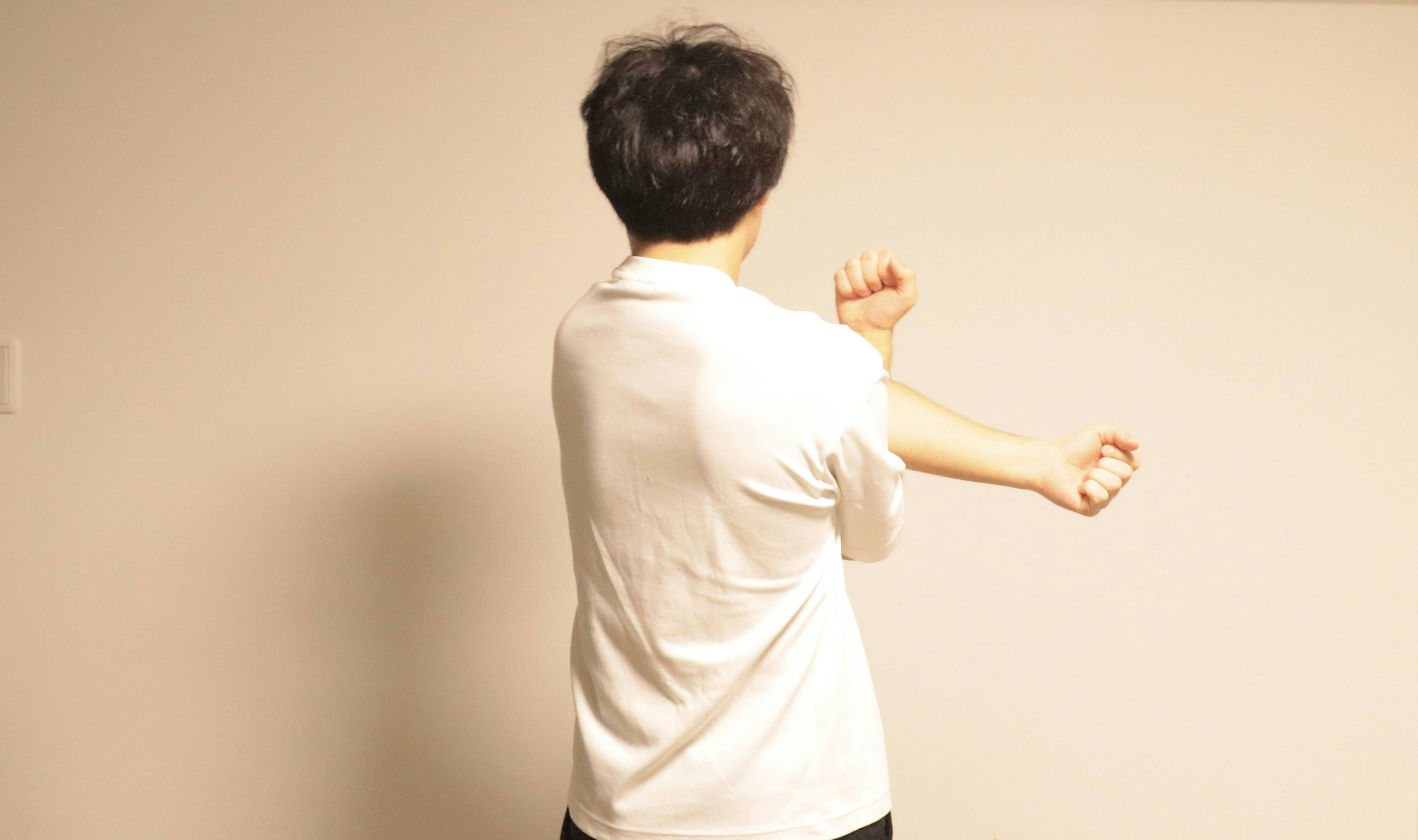 Person in white t-shirt stretching their arm seen from behind