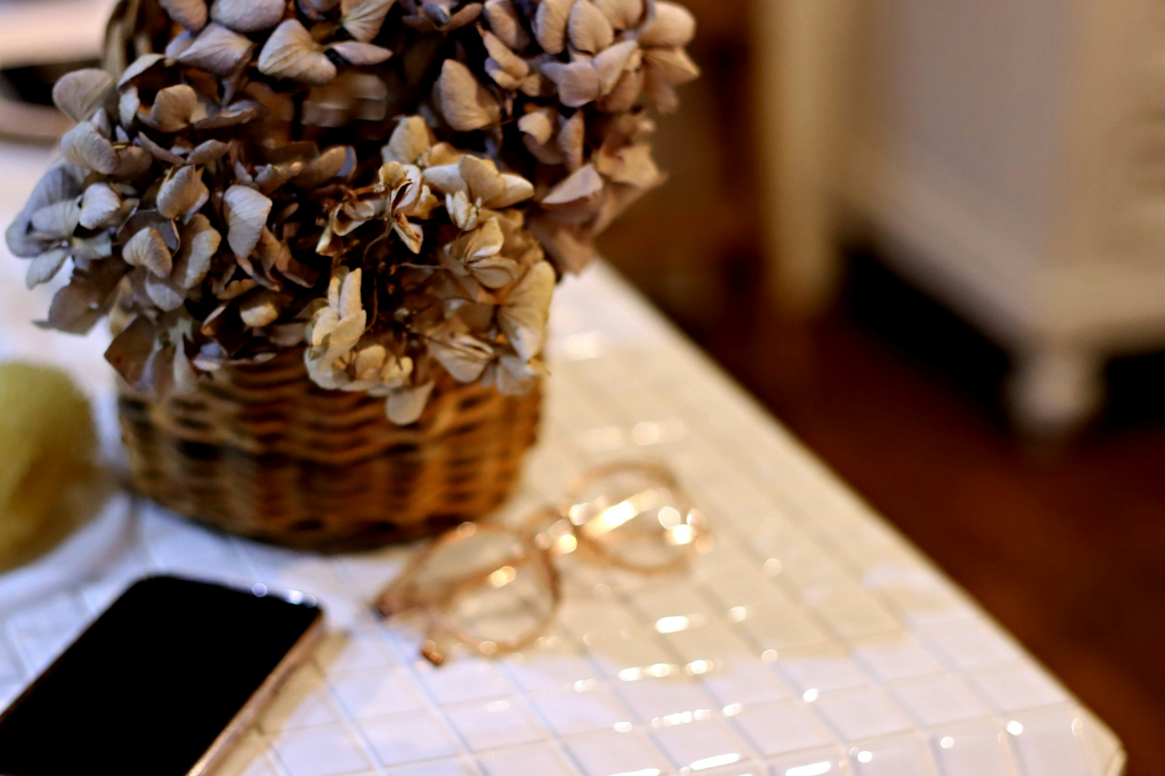 Floral arrangement in a basket on a table with glasses and a phone