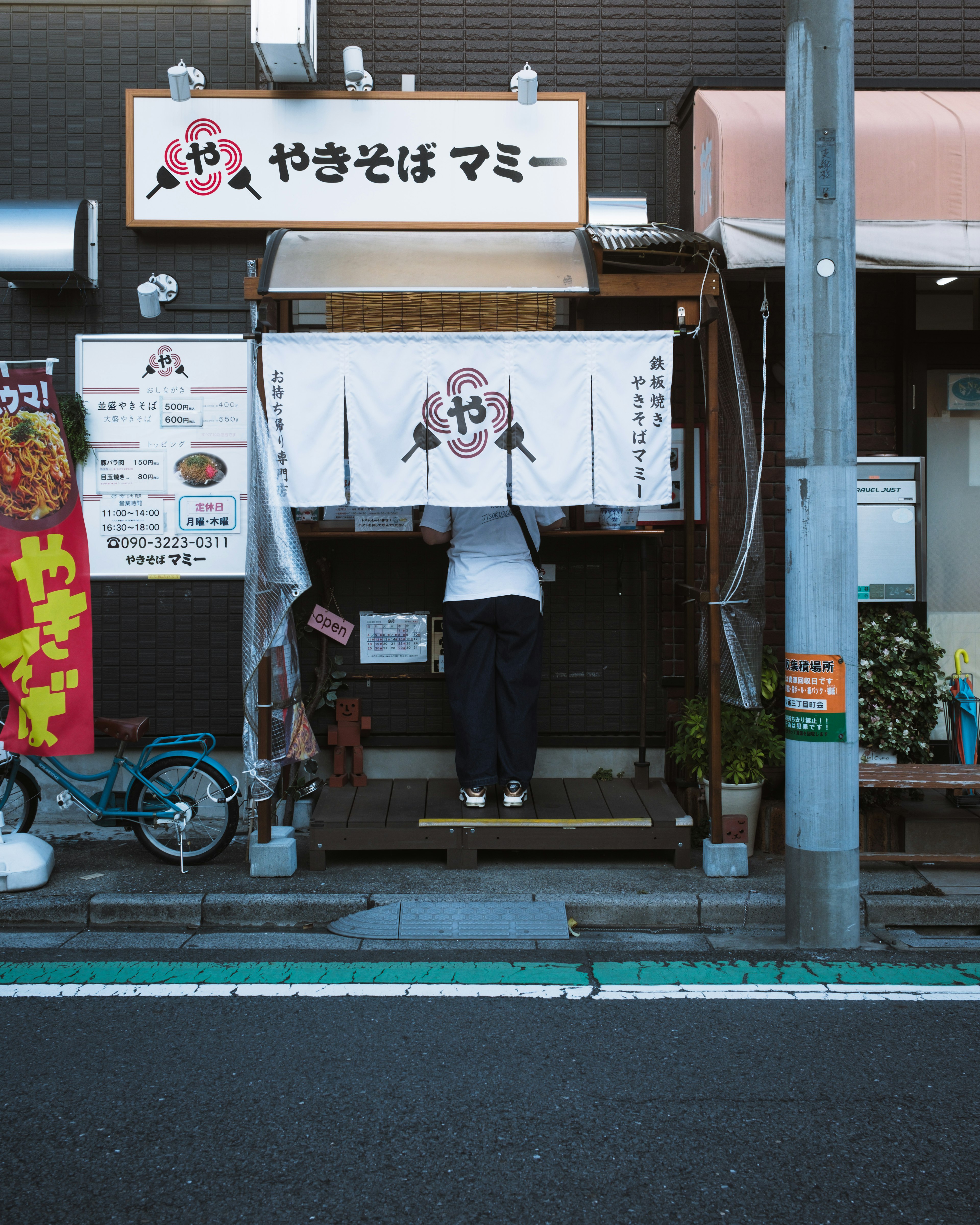 Seorang pekerja di depan kedai ramen dengan eksterior yang khas