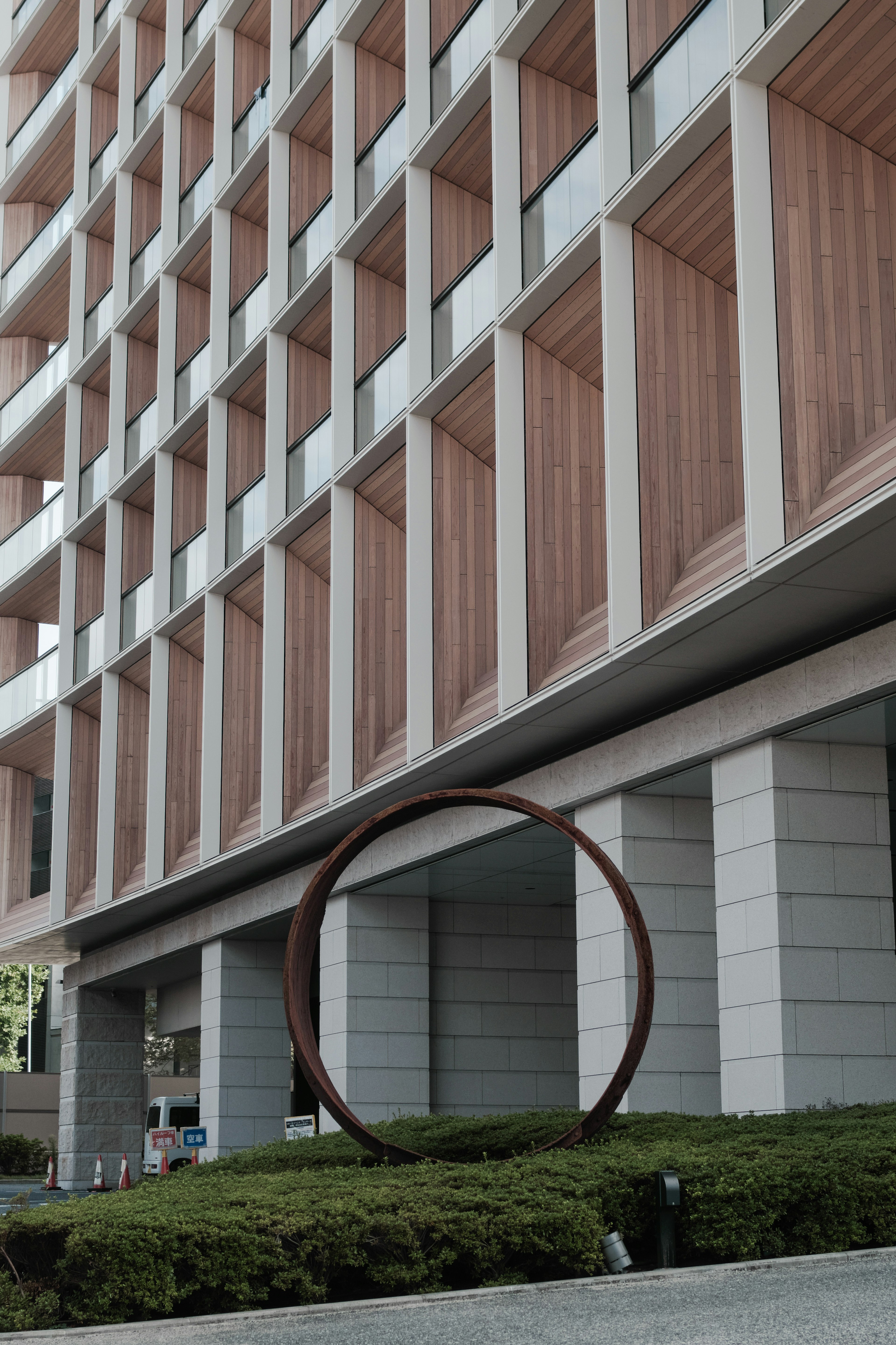 Modern building facade featuring a circular sculpture and green landscaping