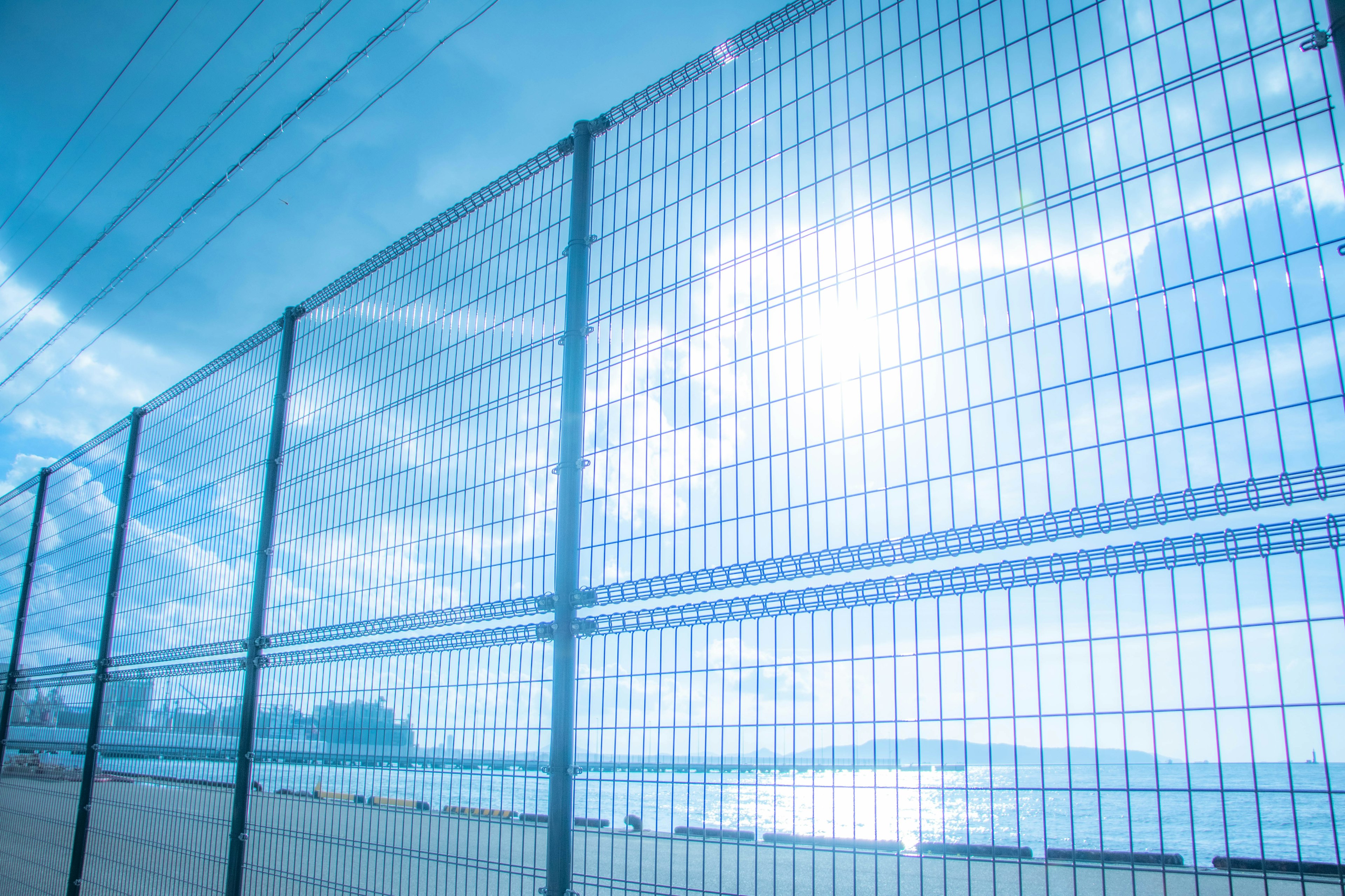 Metallzaun mit blauem Himmel und Sonnenlicht im Hintergrund