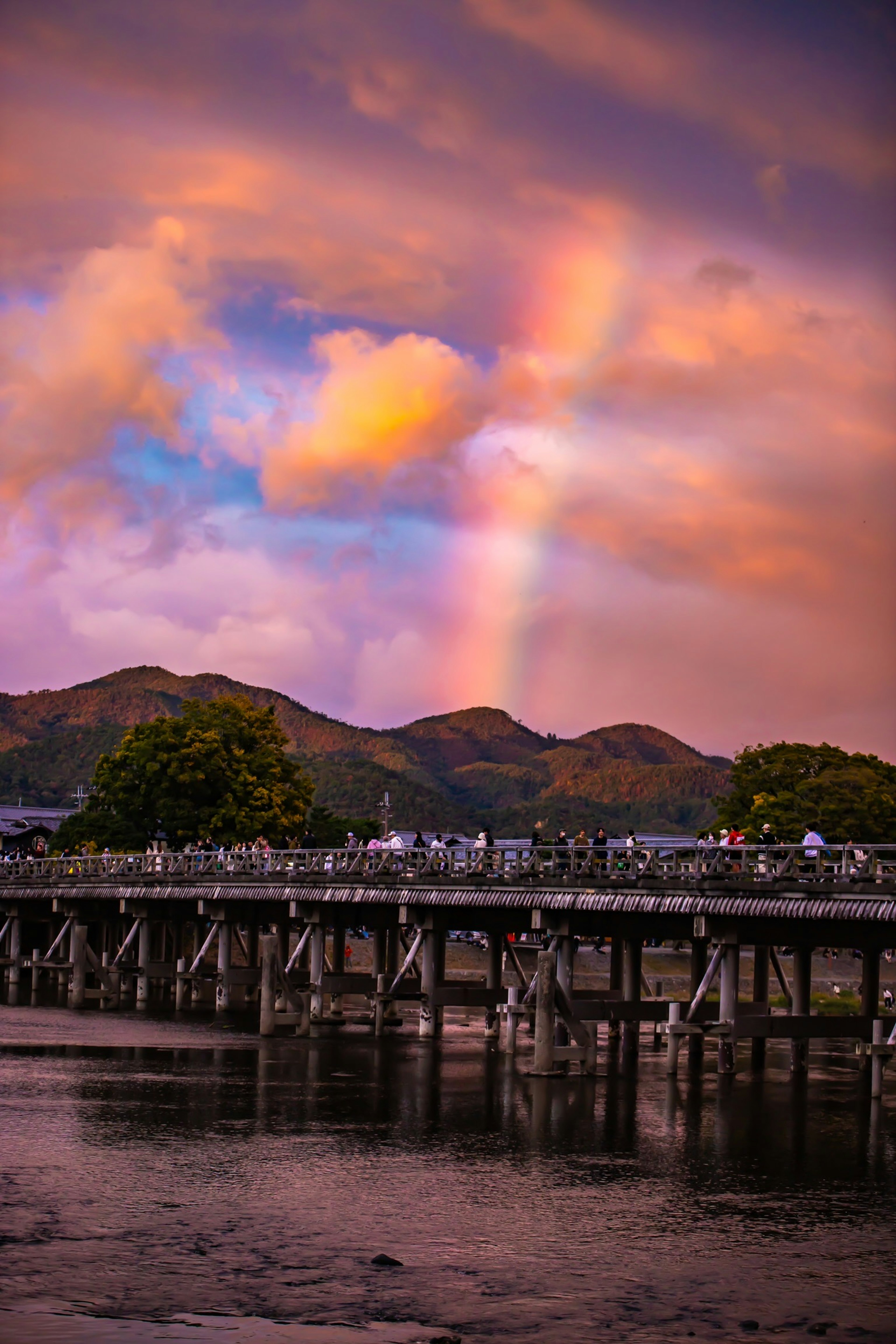 Scenic view of a pier under a sunset sky with a rainbow and mountains in the background