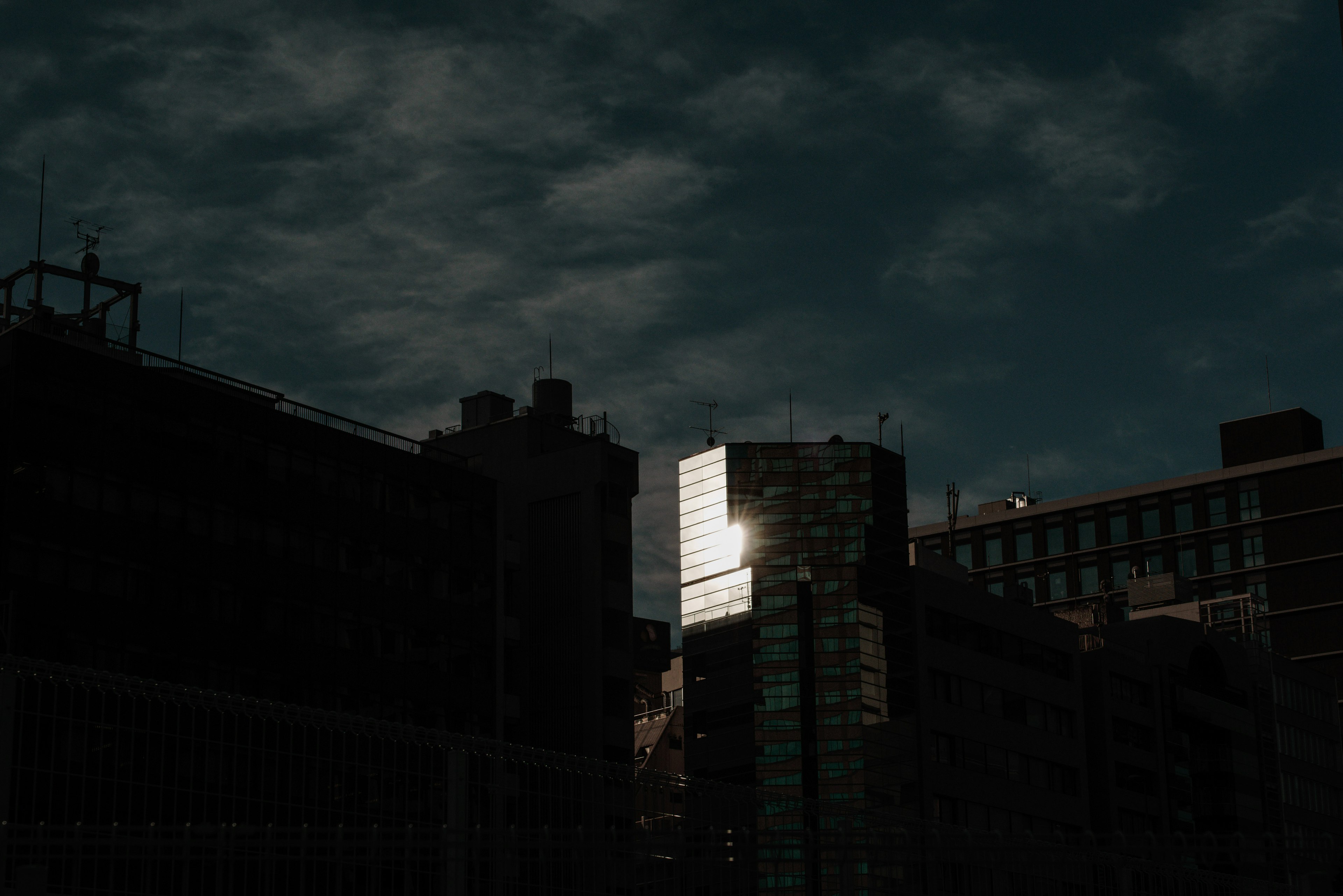 Silhouetted buildings against a dark sky with a bright reflection on glass