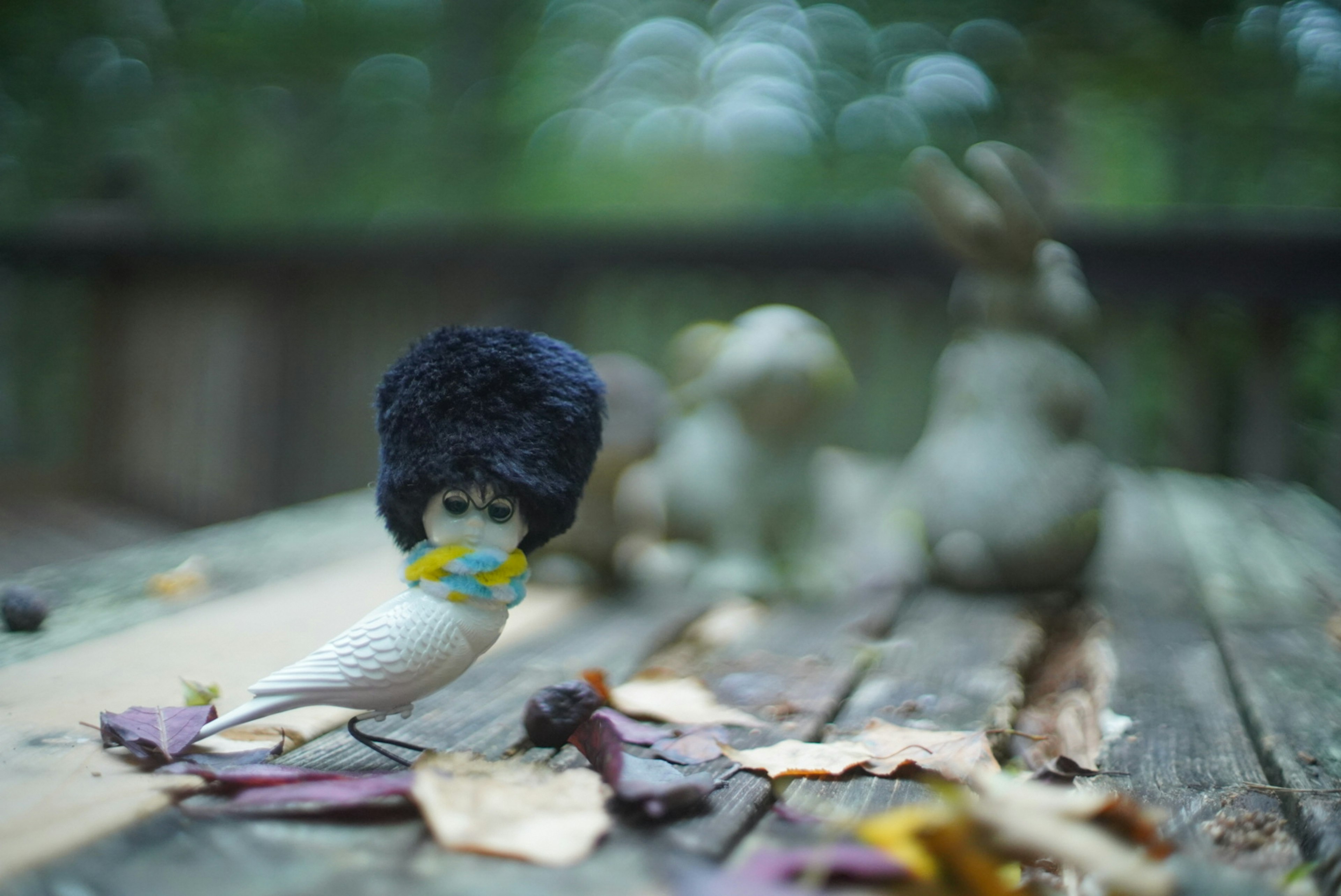 Sebuah patung burung unik mengenakan topi hitam di atas meja kayu dengan patung kelinci di latar belakang