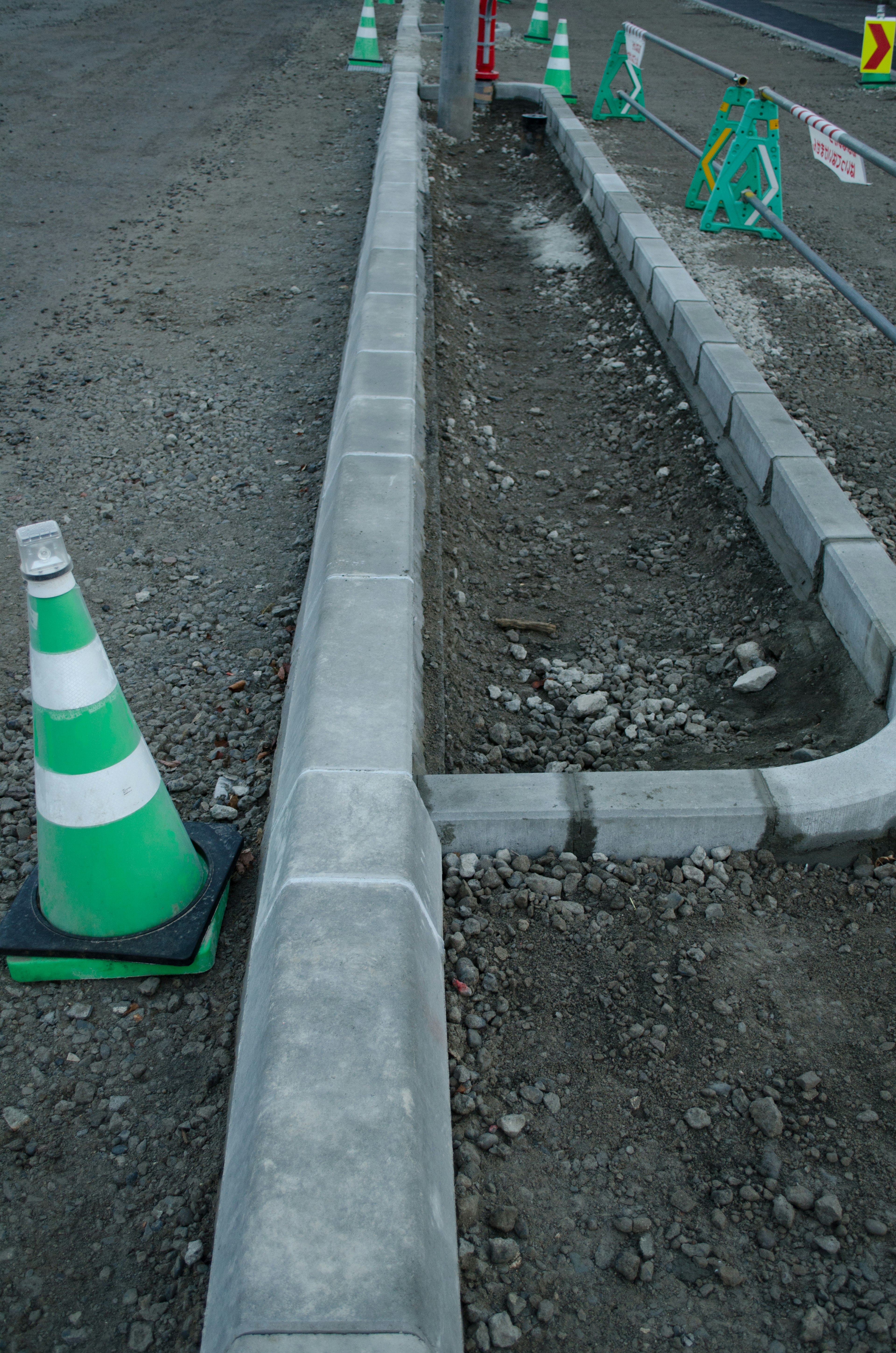 Situs konstruksi dengan trotoar beton dan kerucut lalu lintas hijau