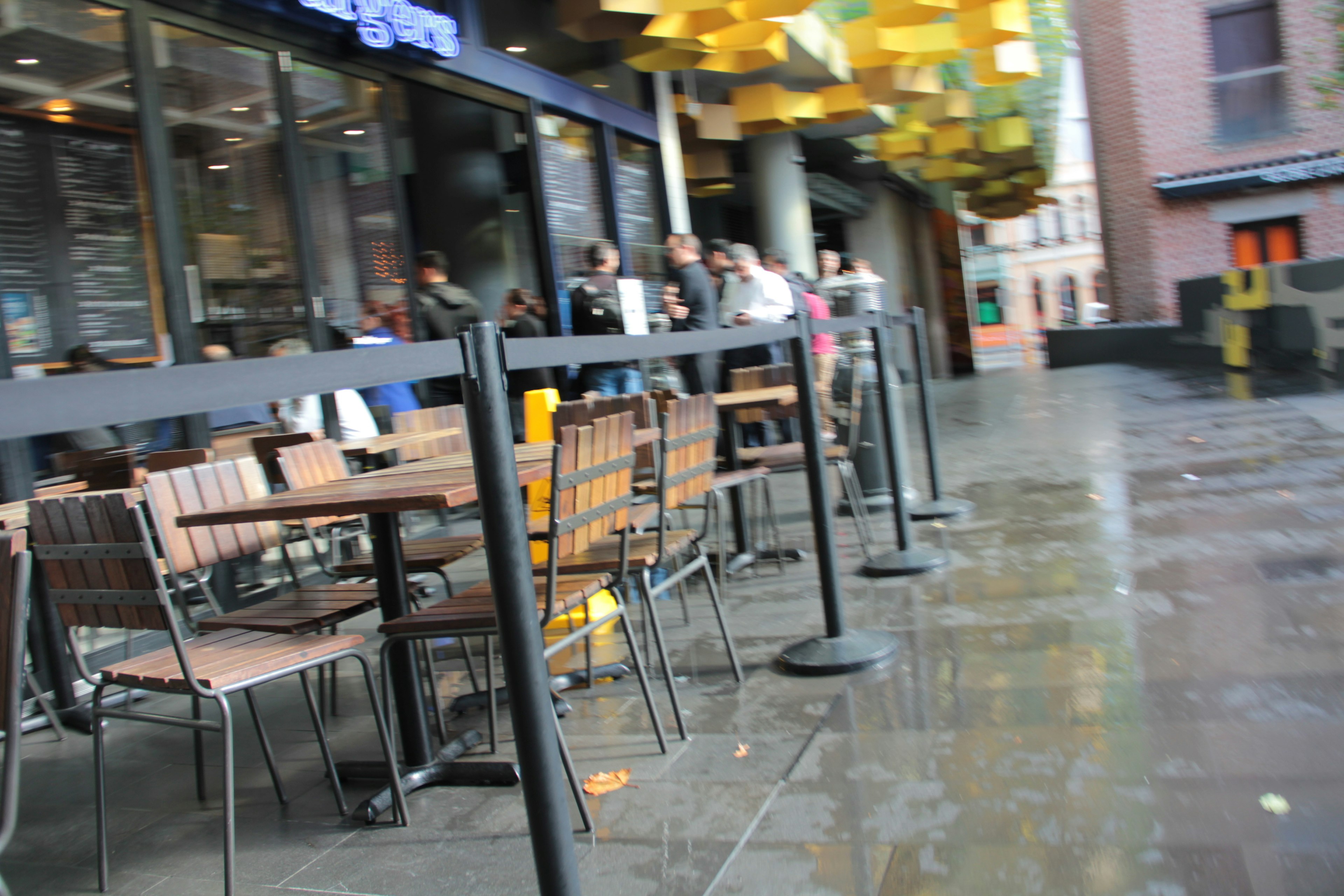 Outdoor cafe seating with wooden tables and chairs wet ground under rainy conditions yellow decorative elements