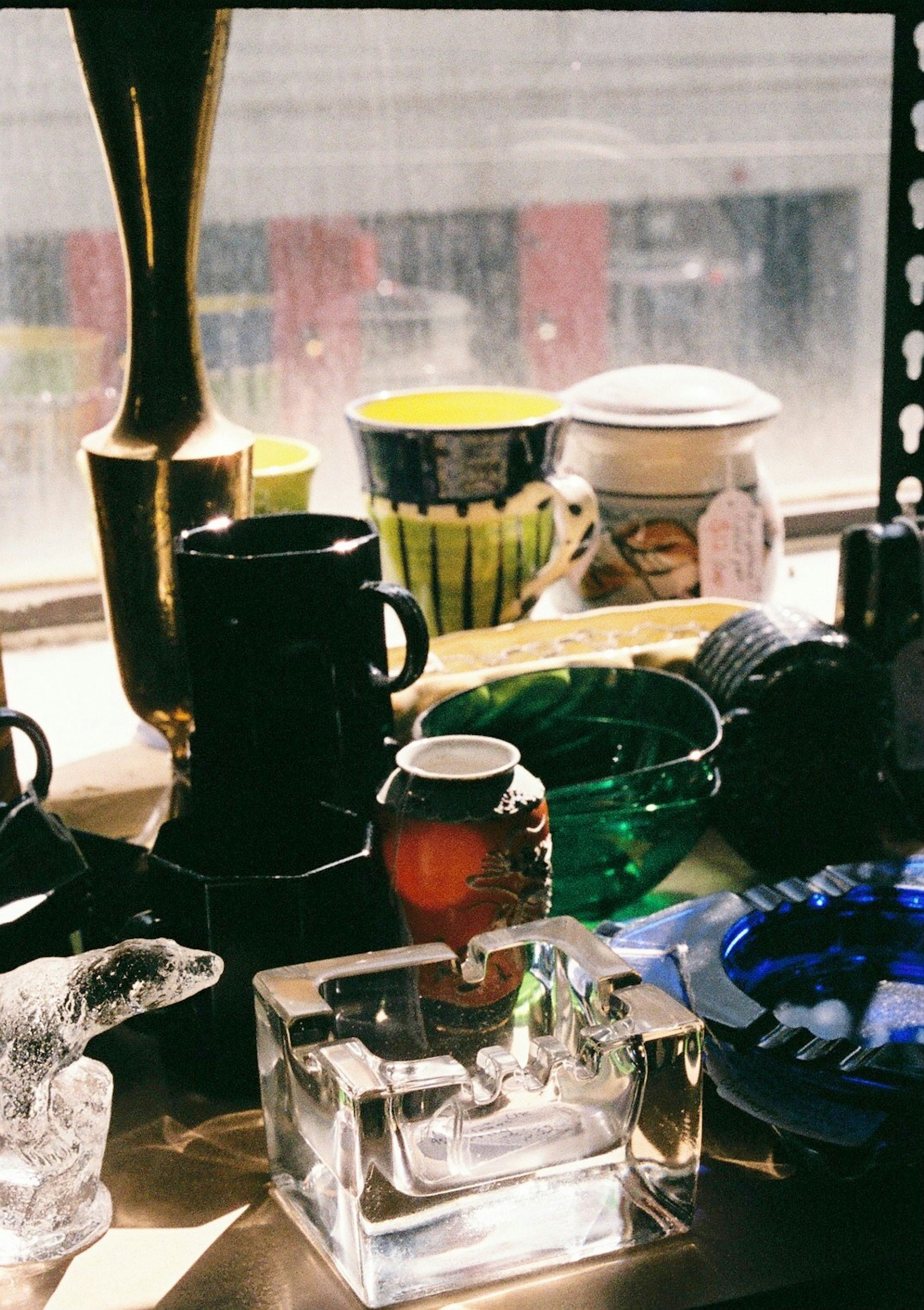 A collection of diverse glassware and ceramics displayed by a window