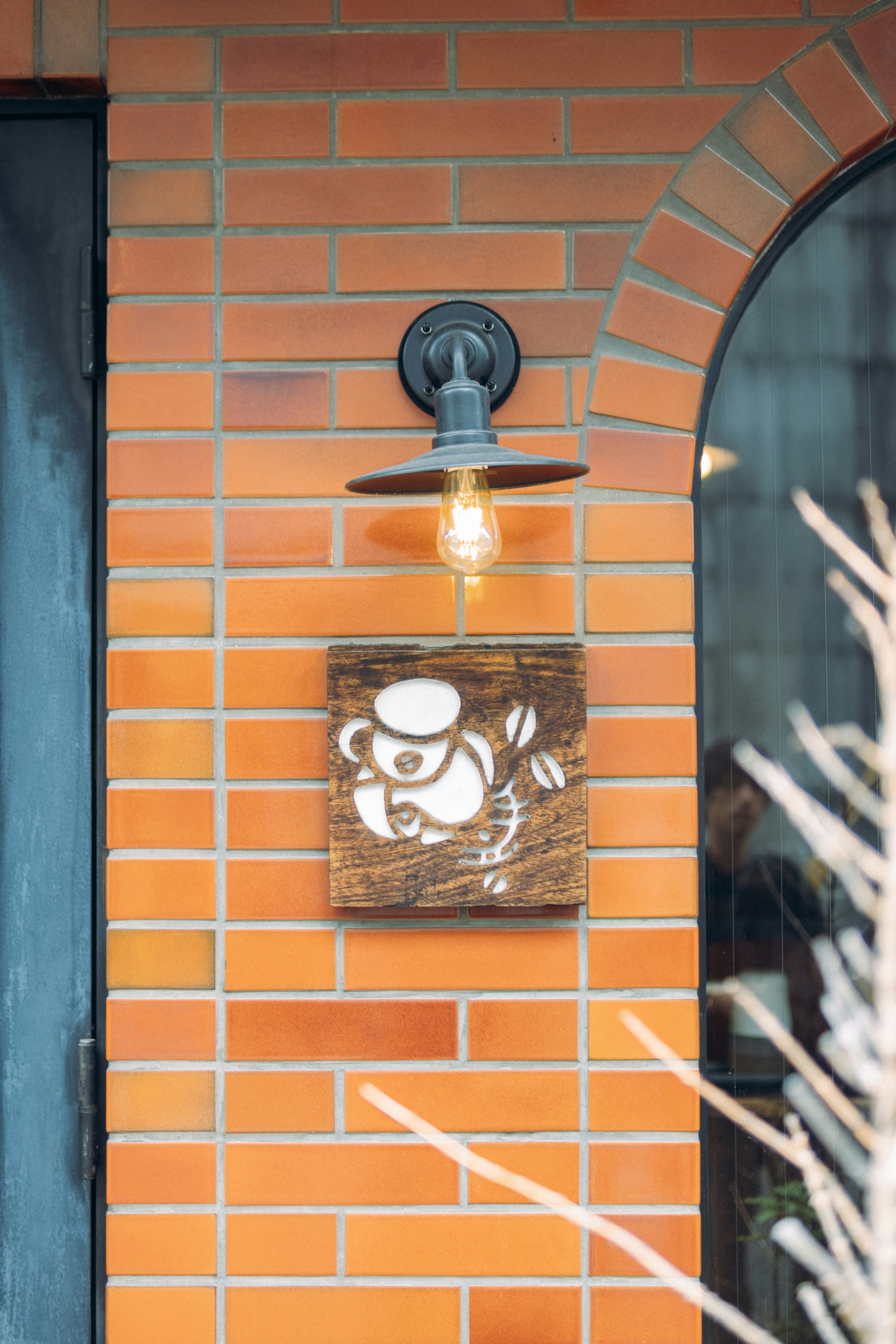 Wooden sign with panda illustration under light fixture on brick wall