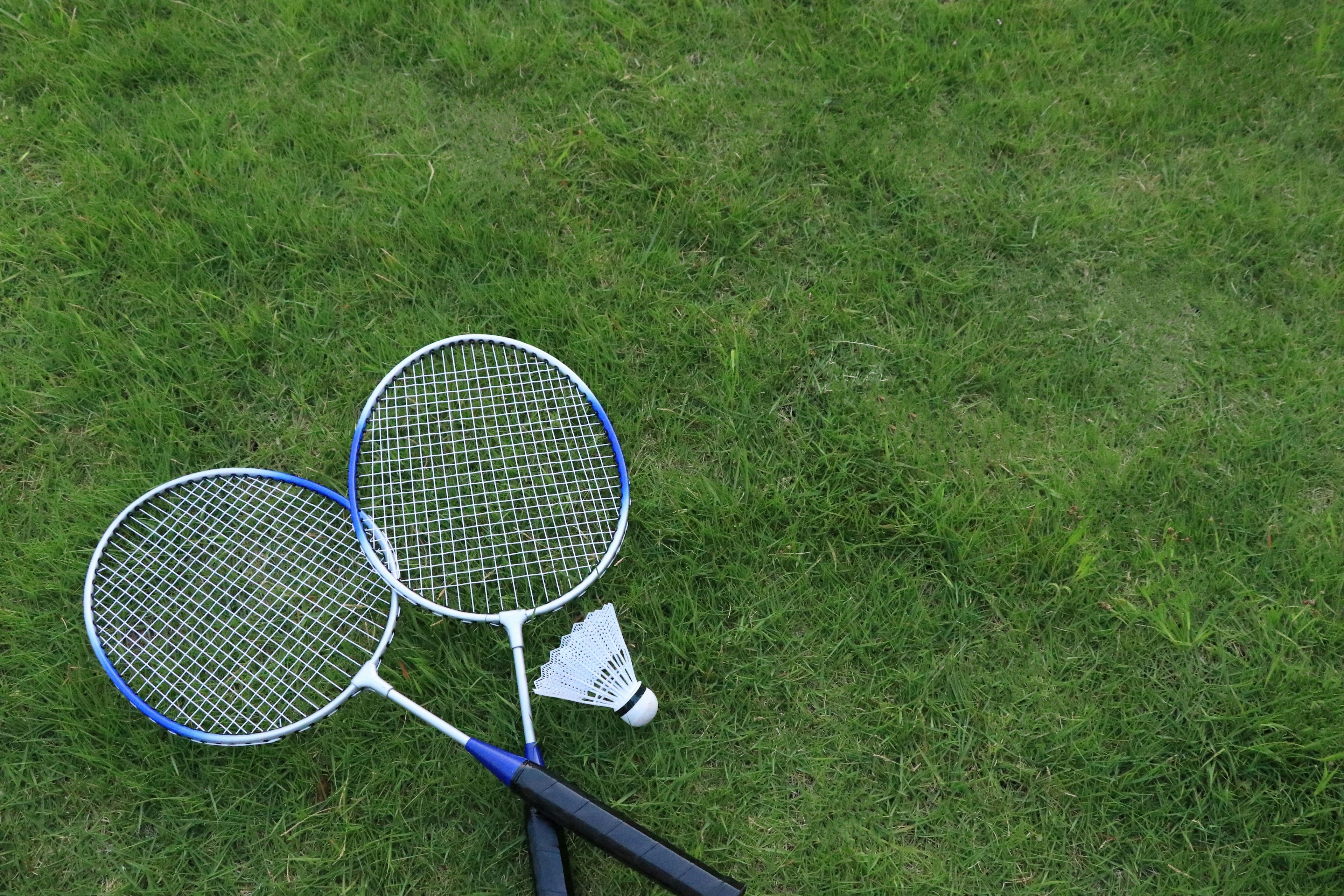 Dua raket dan satu shuttlecock tergeletak di atas rumput hijau