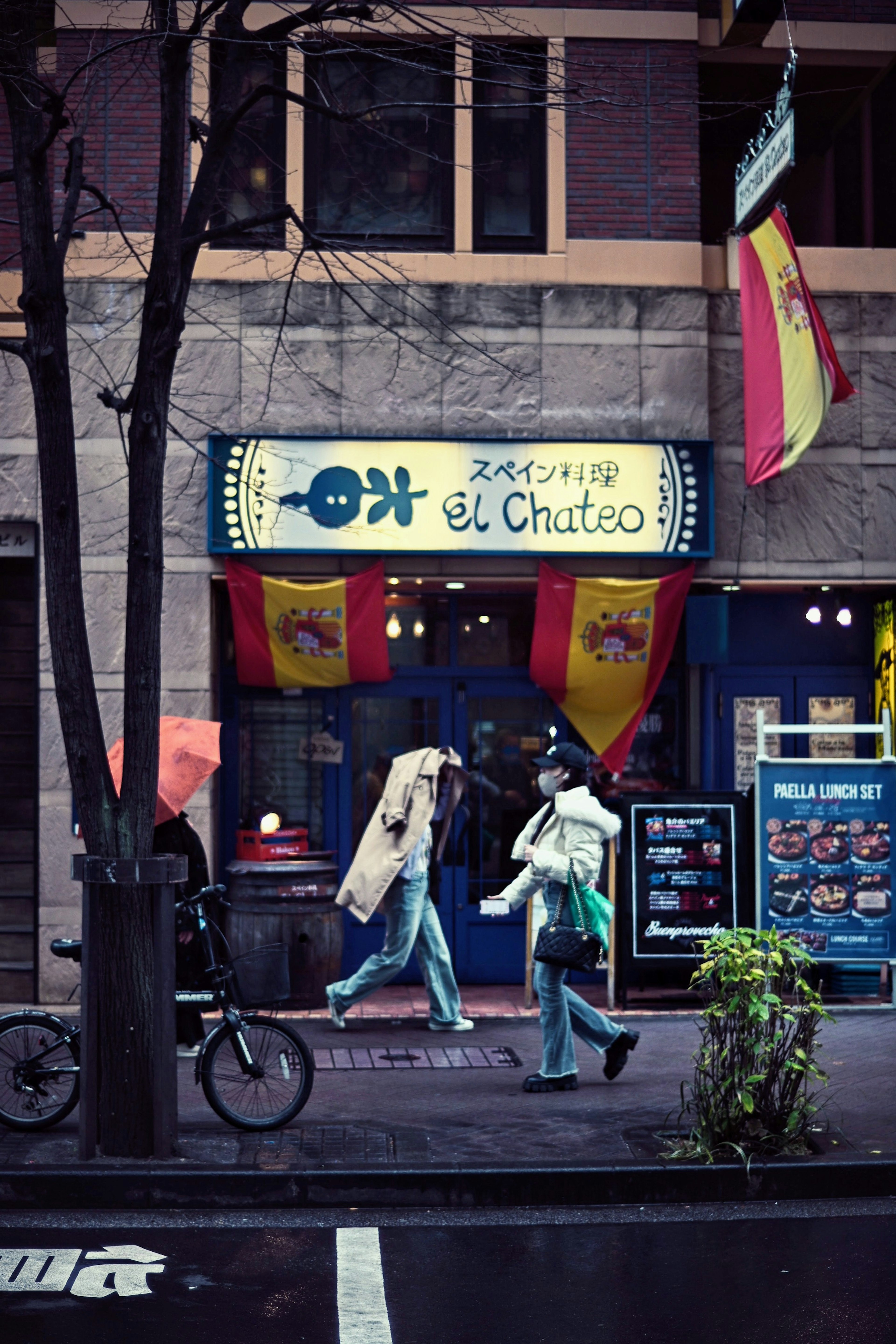 Exterior of a restaurant with a colorful sign featuring the name el Chateo two people walking by