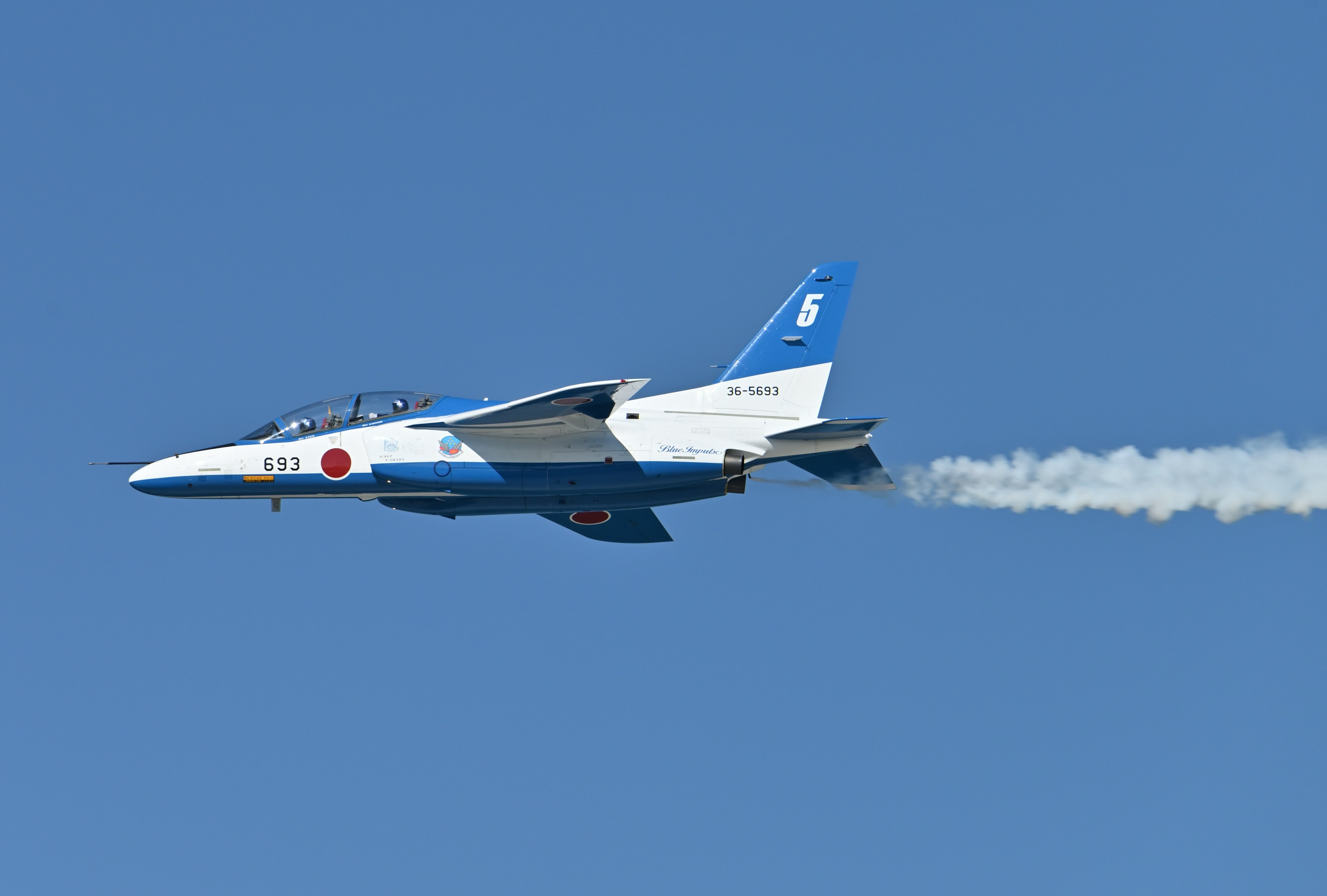 Caza japonés volando contra un cielo azul con una estela de humo blanco