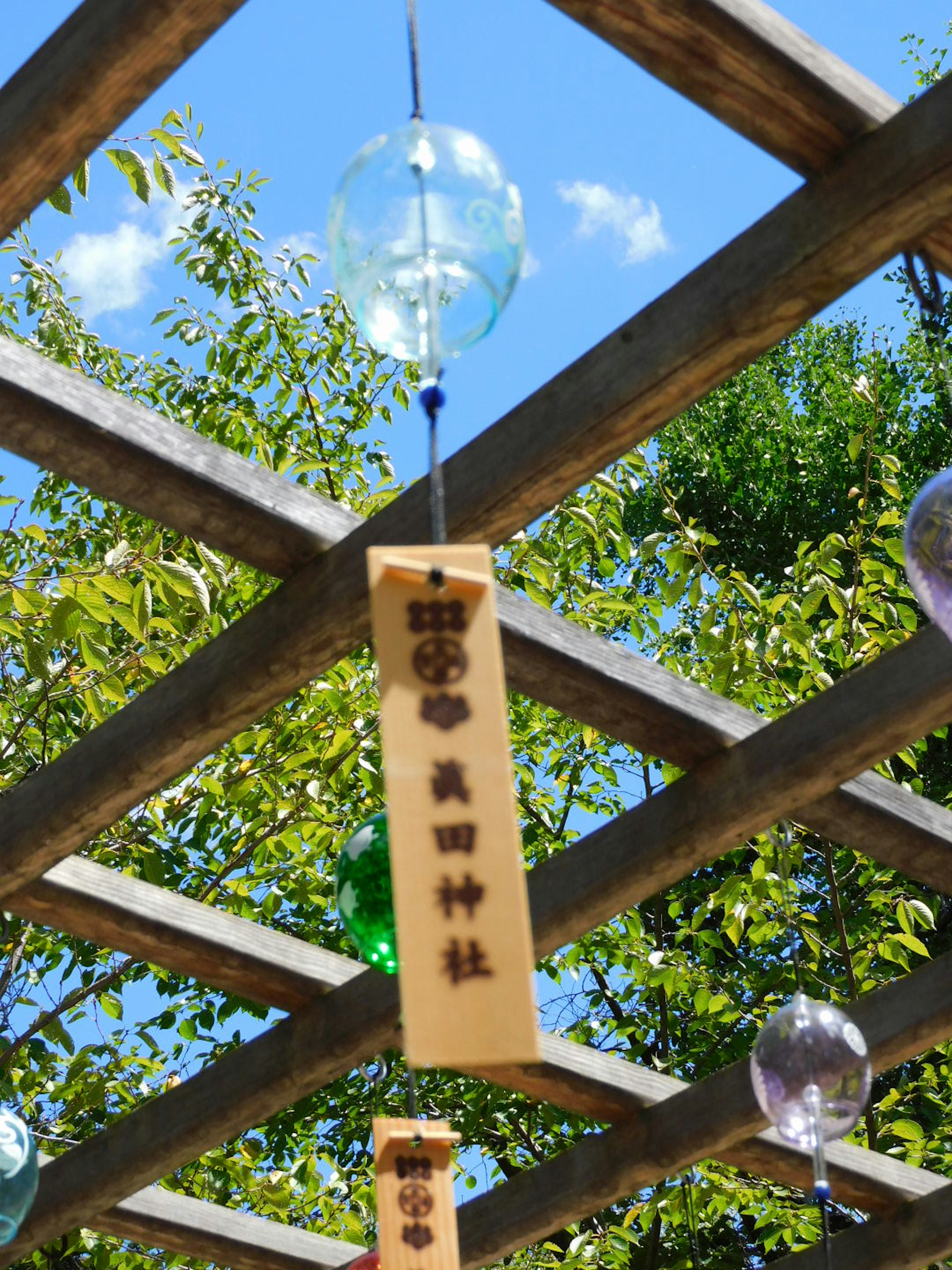 Windspiele und Holztafel hängen unter einem blauen Himmel