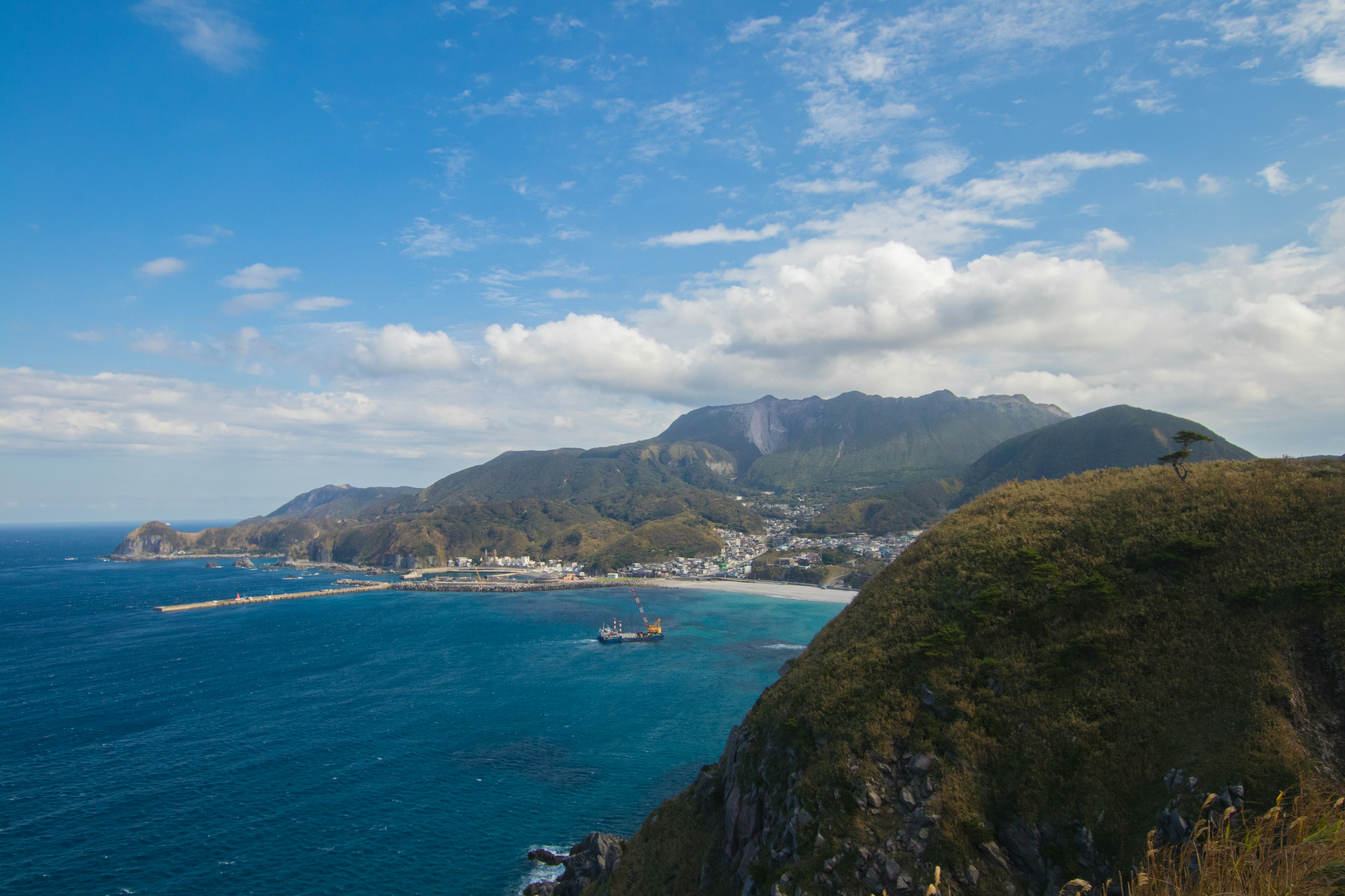 Scenic view of mountains and a coastal town under blue sky and white clouds