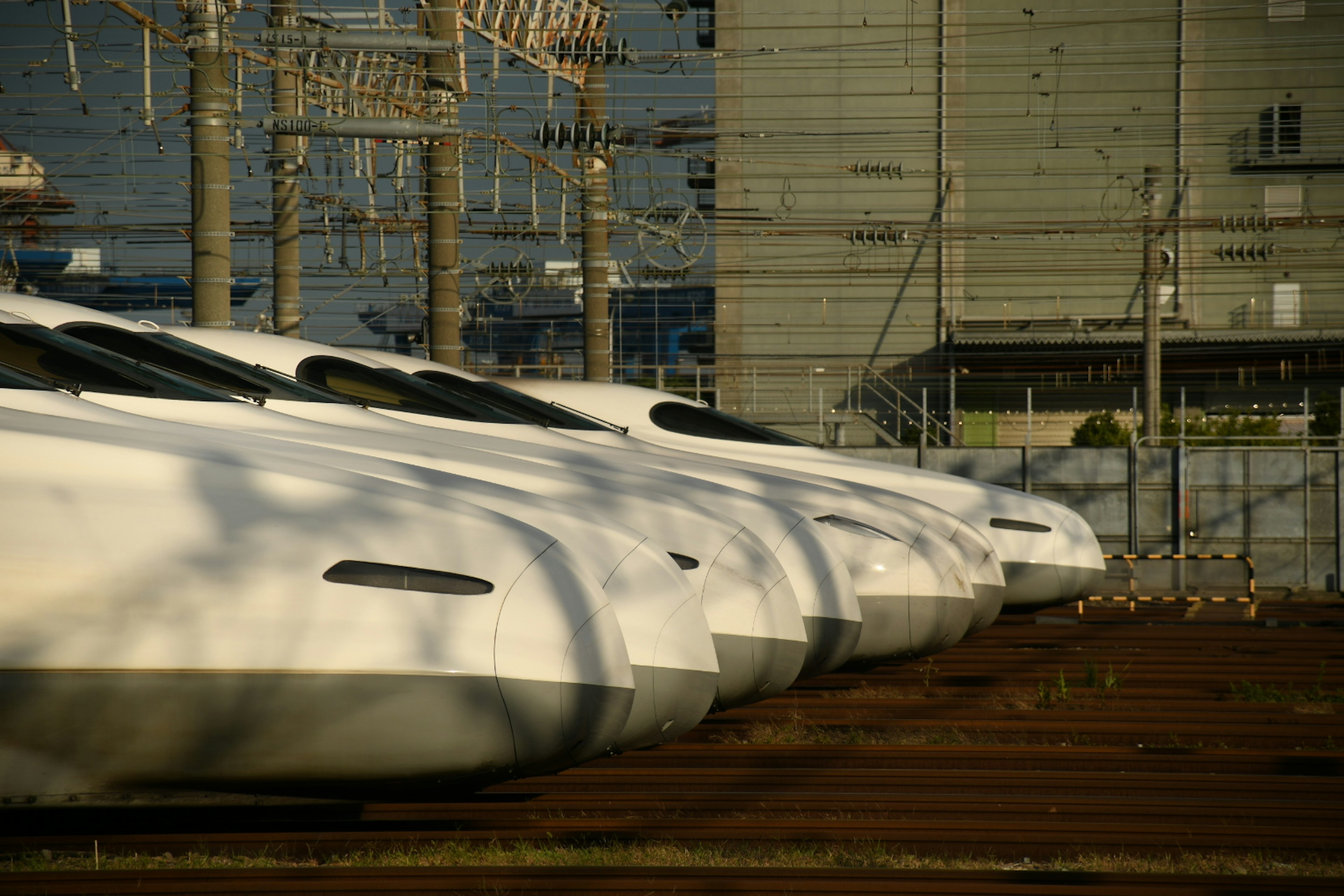 新幹線の車両が並んでいる風景で、背景には電線と建物が見える