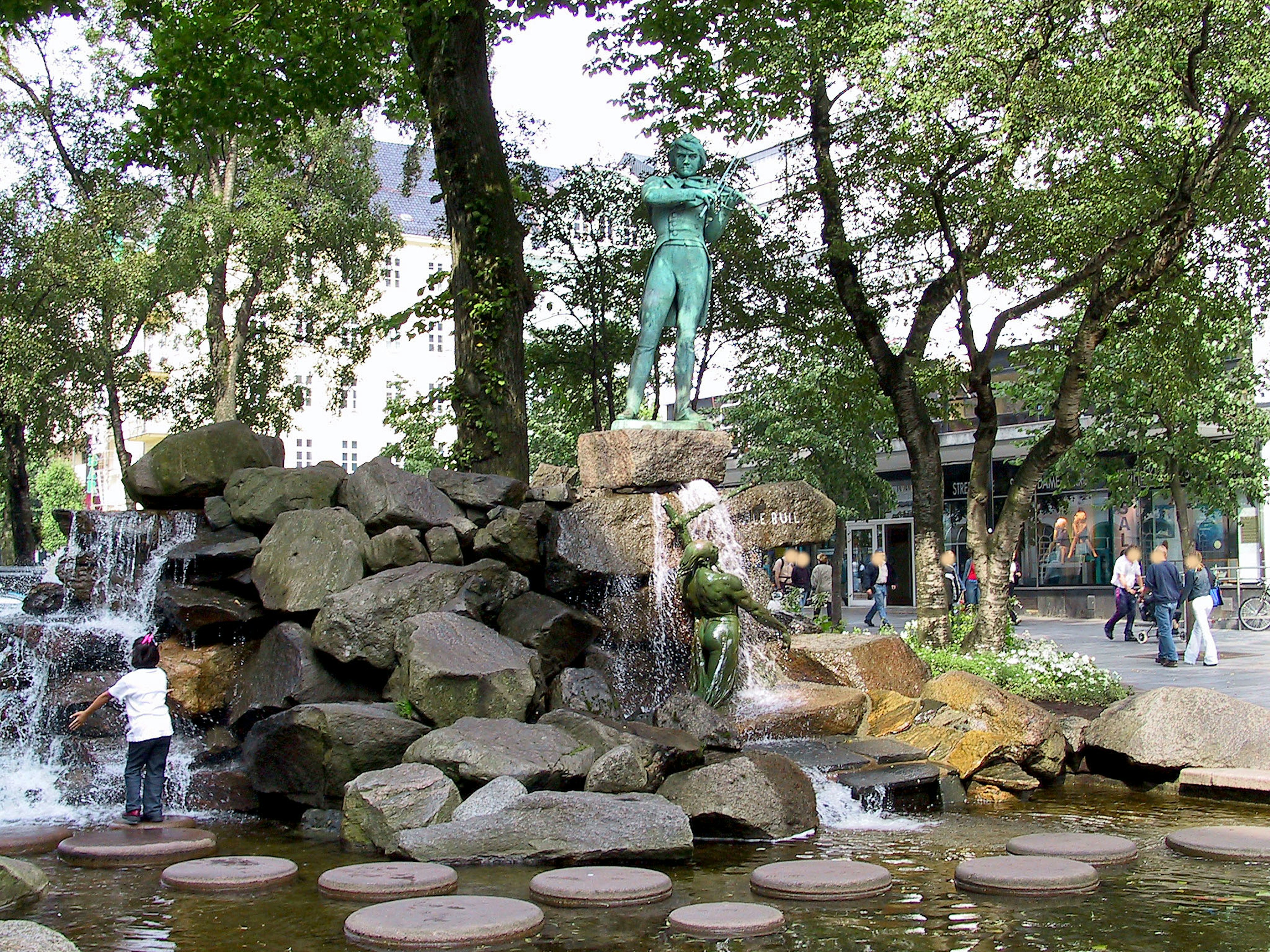 Fontaine avec statue verte entourée d'arbres et de personnes