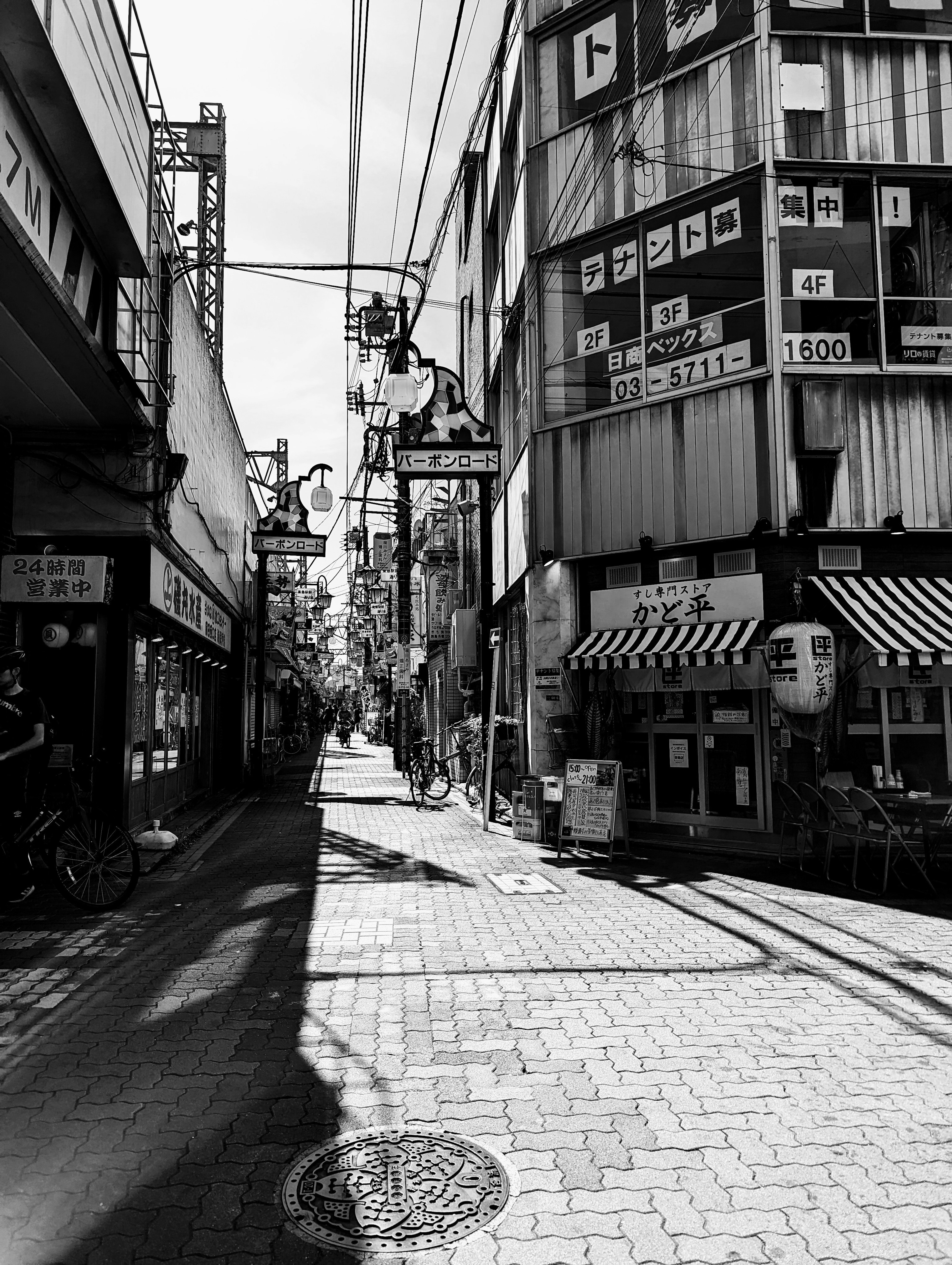 Black and white view of a narrow street lined with commercial buildings and shops