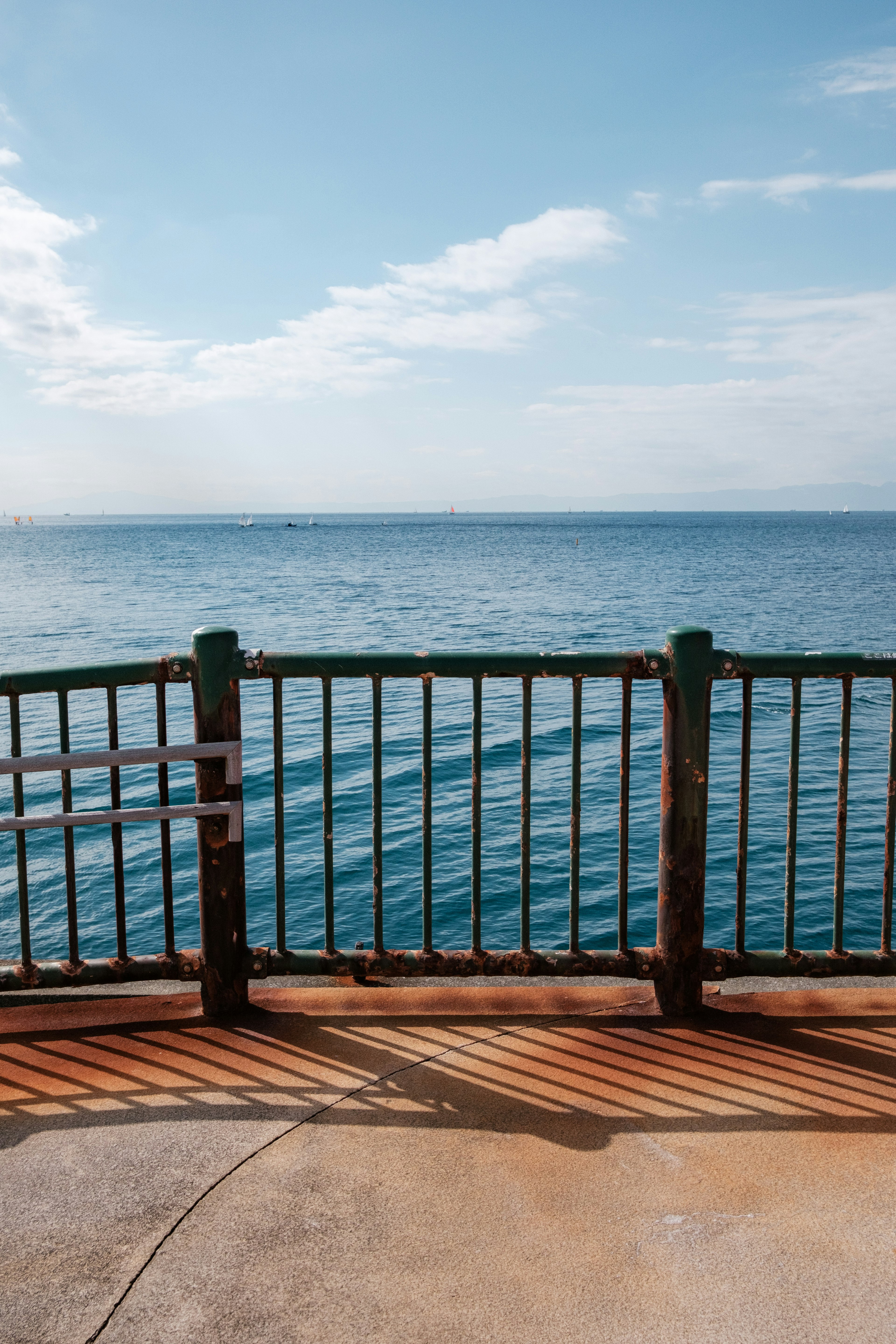 Eine Sicht auf den blauen Ozean und weiße Wolken mit einem Geländer an einem Pier