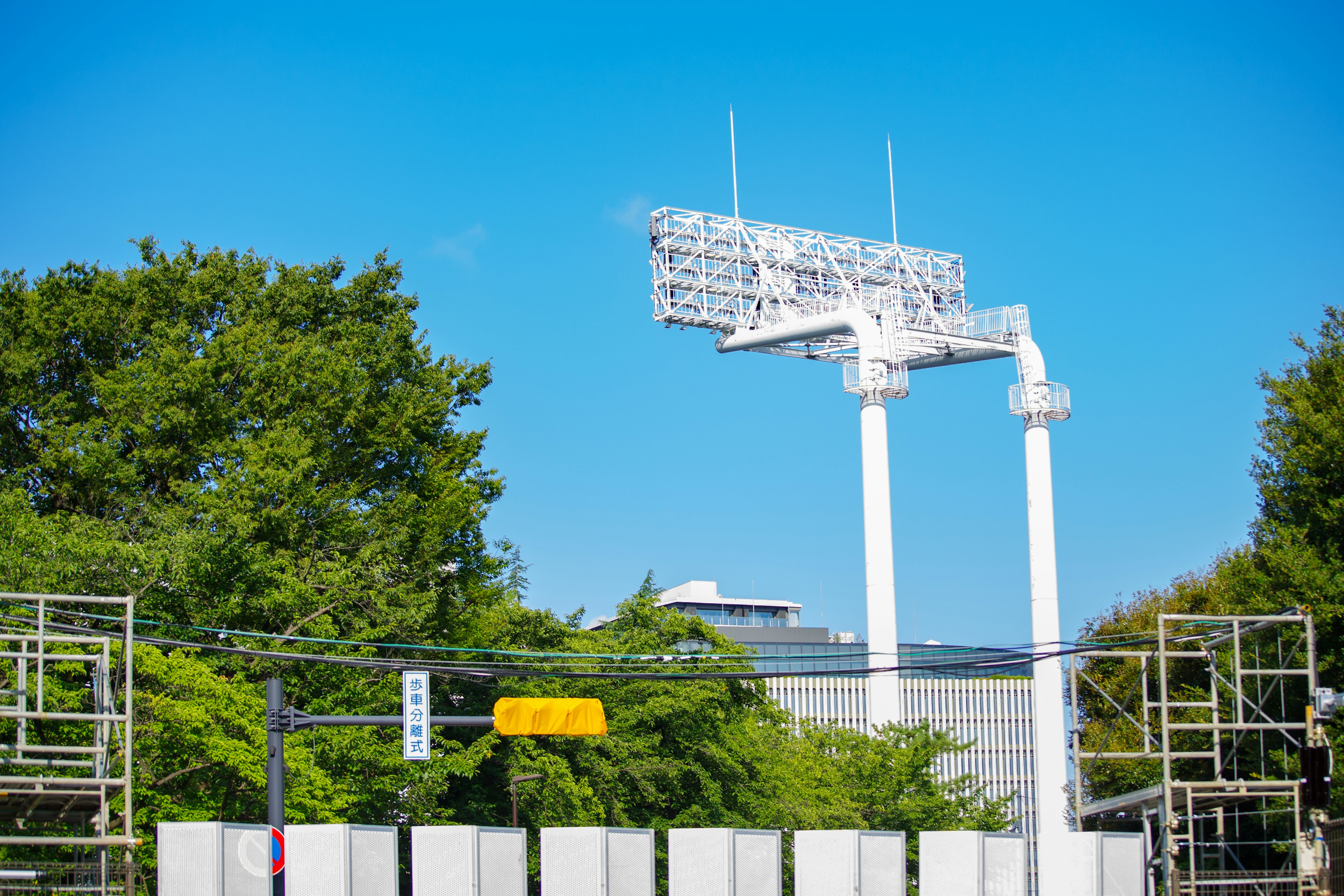 青空の下にある大型の照明塔と周囲の木々