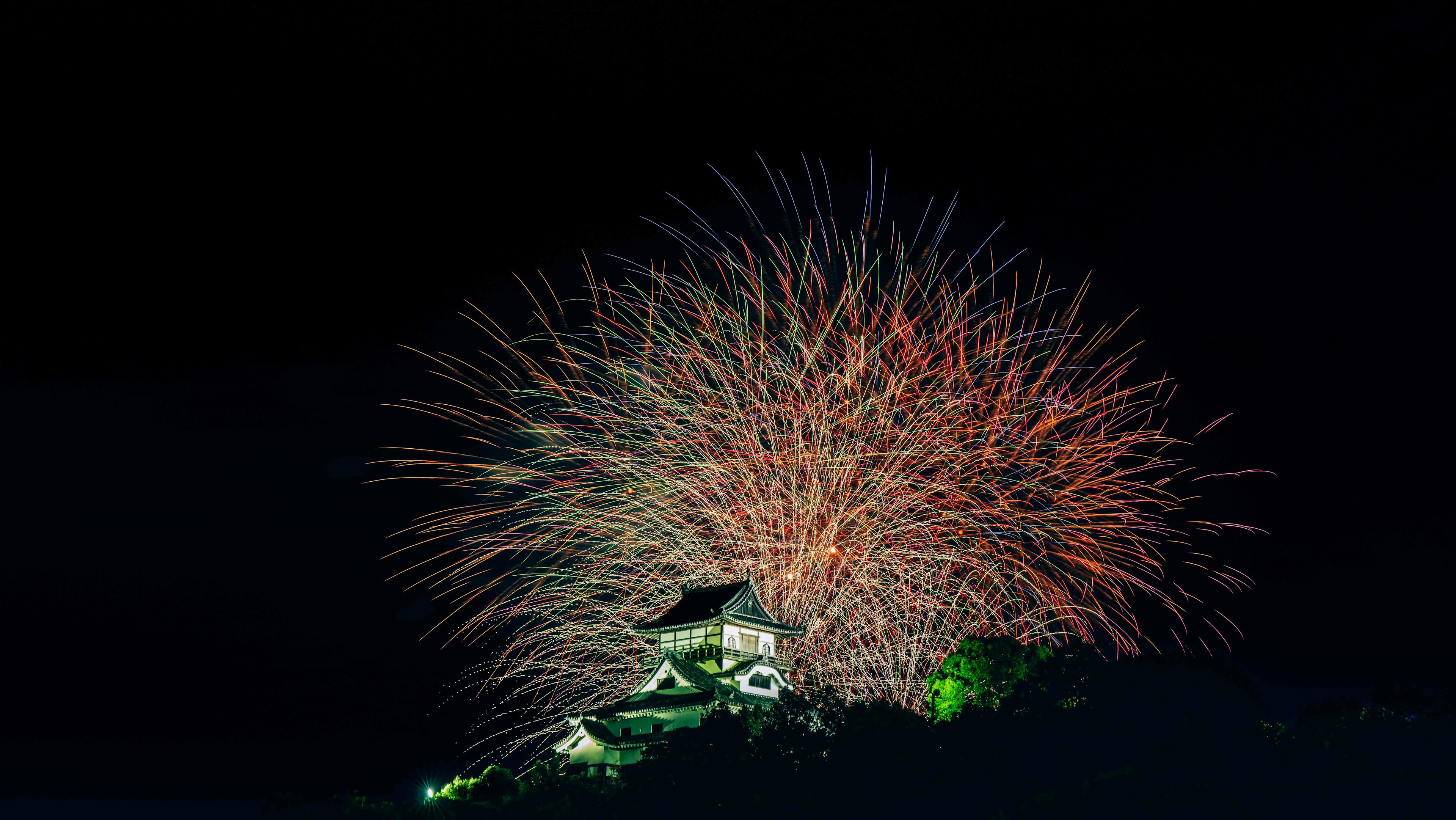 夜空に広がる色とりどりの花火と背景に見える城