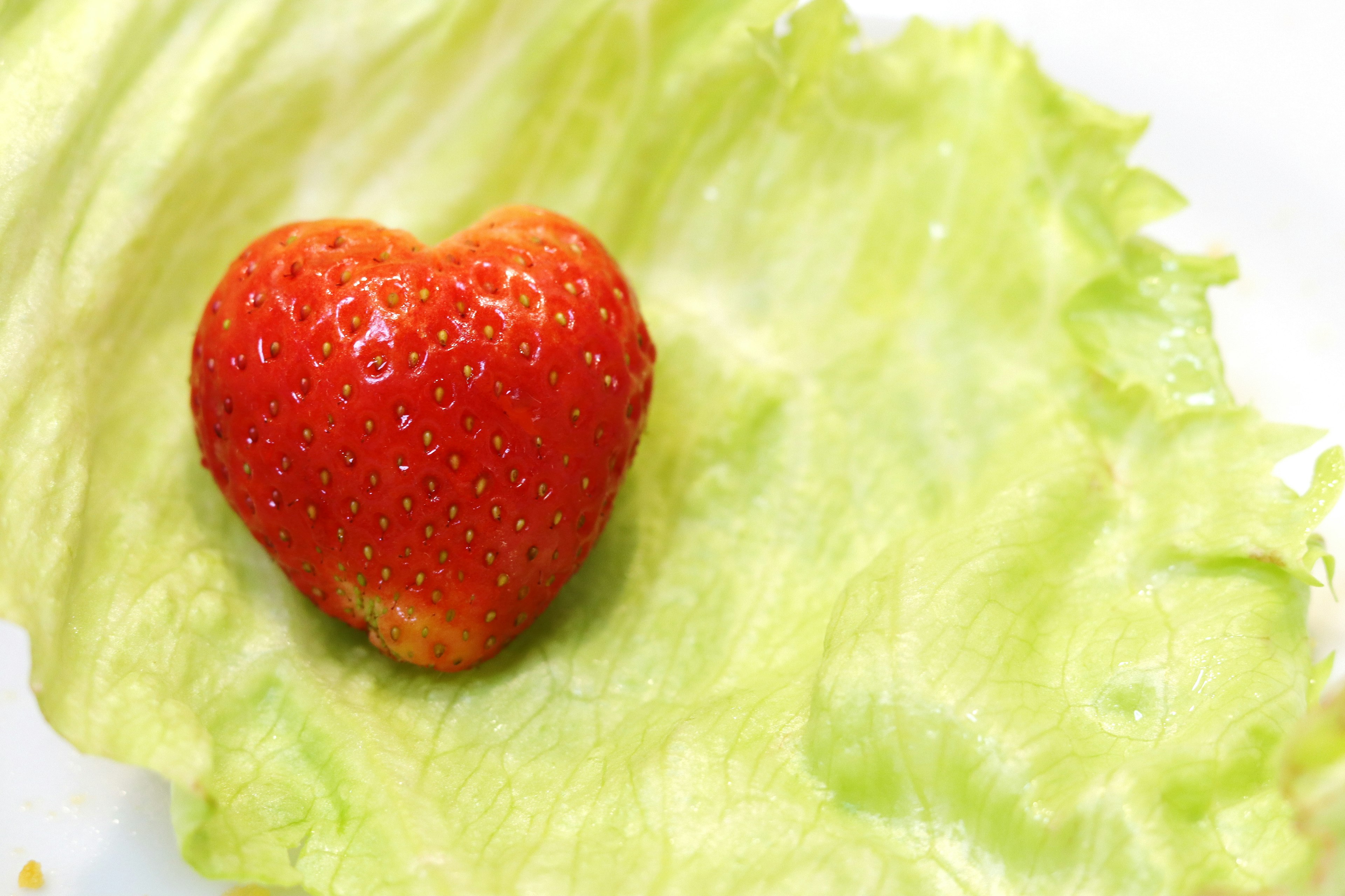 Una fresa en forma de corazón sobre una hoja de lechuga