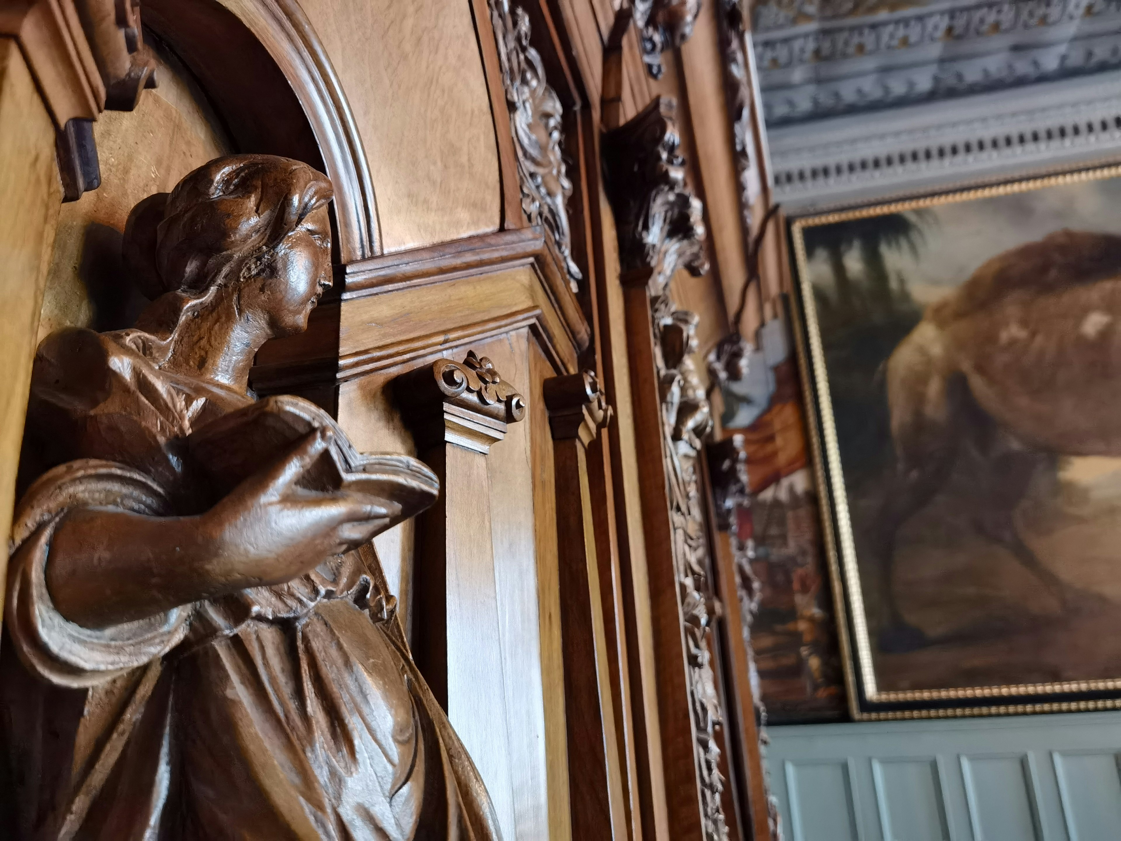 Scultura in legno di una donna su un muro dettagliato con un dipinto sullo sfondo