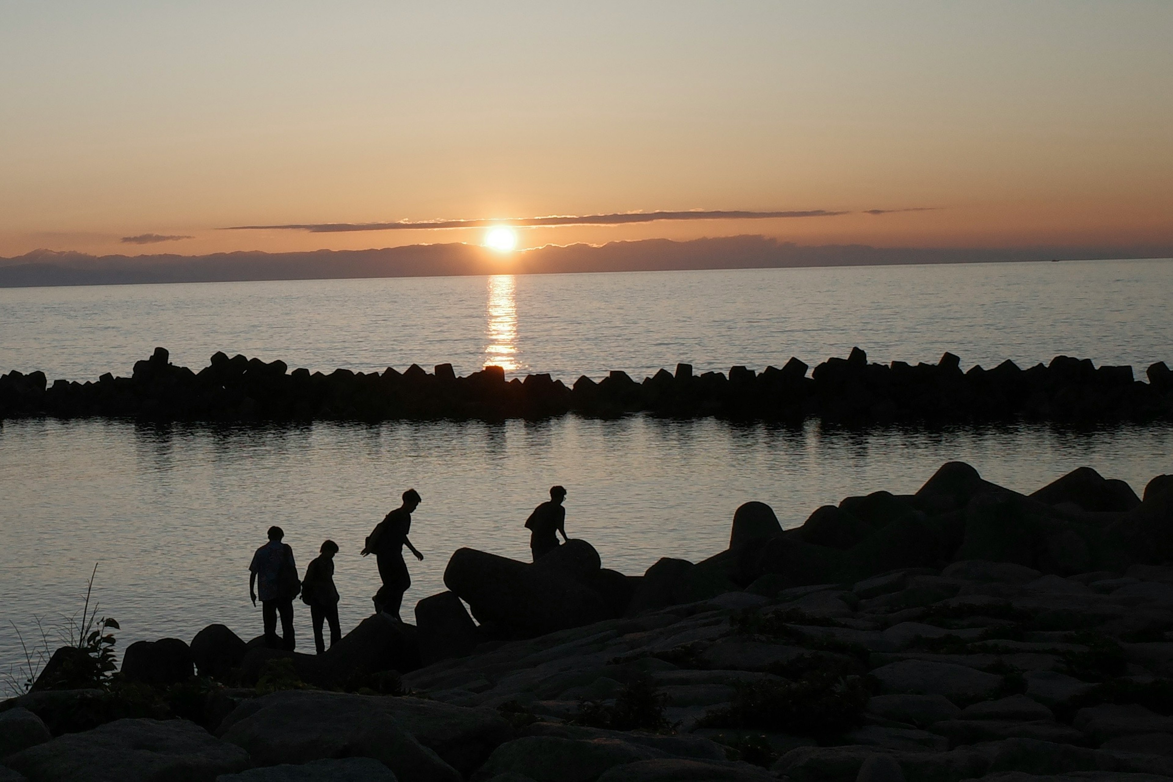 夕日が沈む海岸で人々が岩の上に立っているシルエット