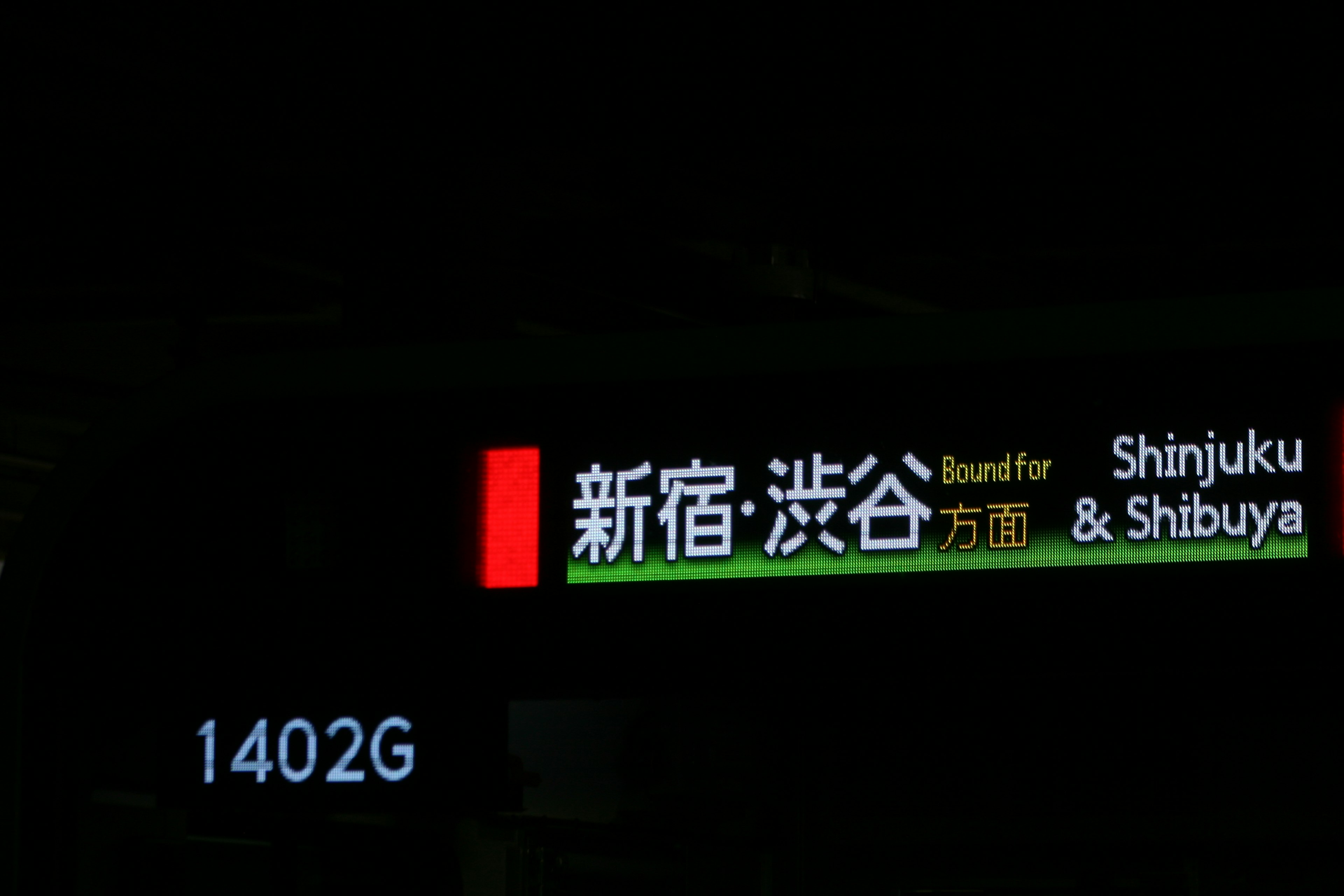 Sign displaying Shinjuku and Shibuya station names bright colors against a dark background