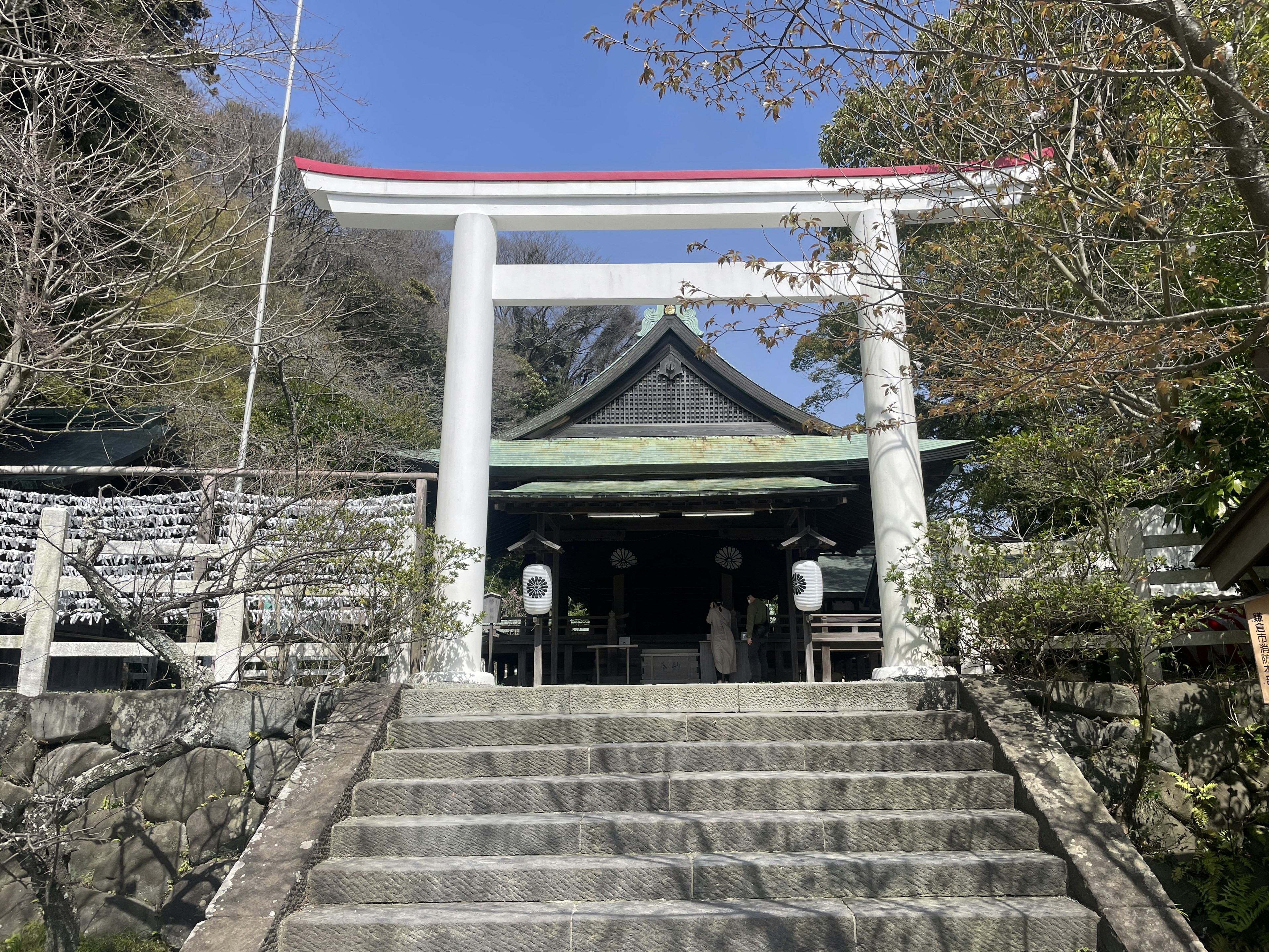 Entrada de un santuario con un torii blanco y un techo verde escaleras de piedra que llevan