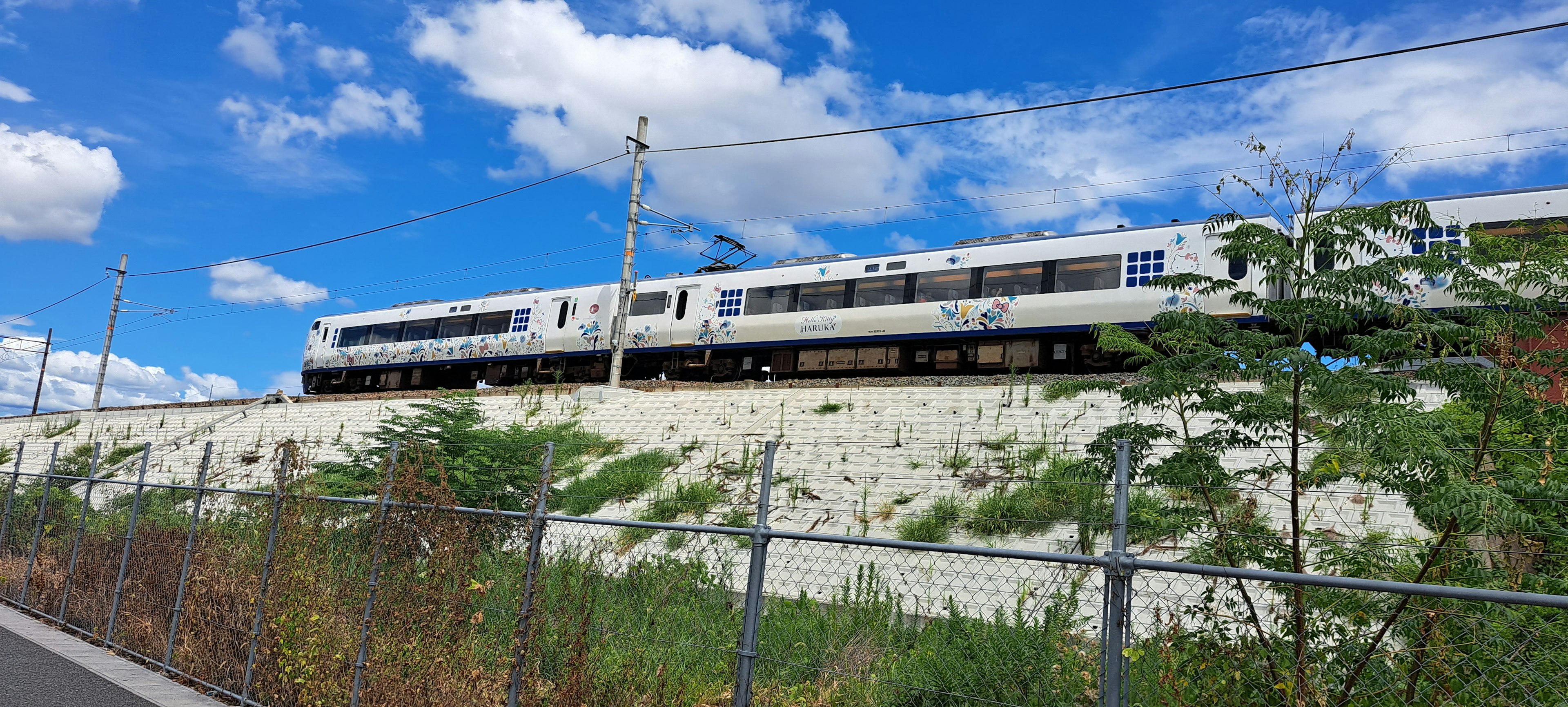 รถไฟสีขาวที่วิ่งไปตามเนินเขาสีเขียวใต้ท้องฟ้าสีฟ้า