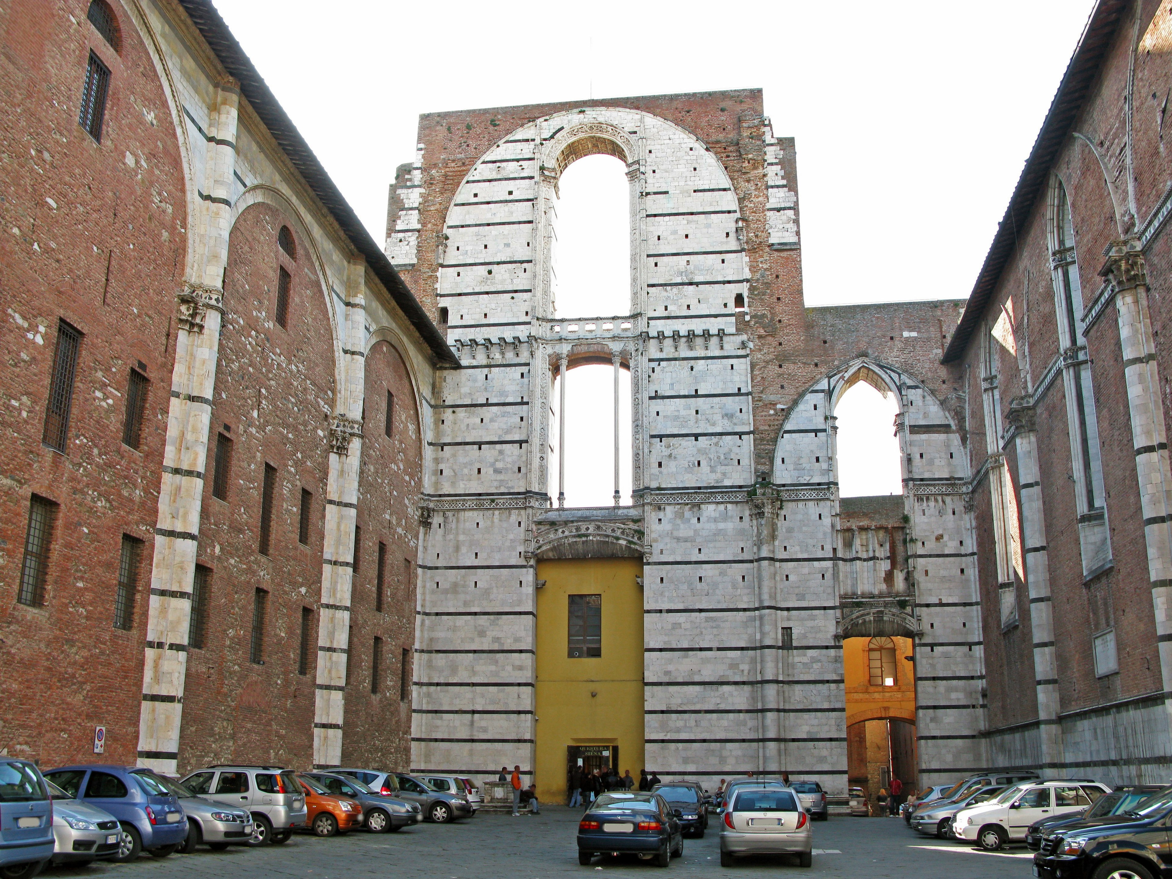 Rovine di una vecchia chiesa con edifici circostanti e auto parcheggiate