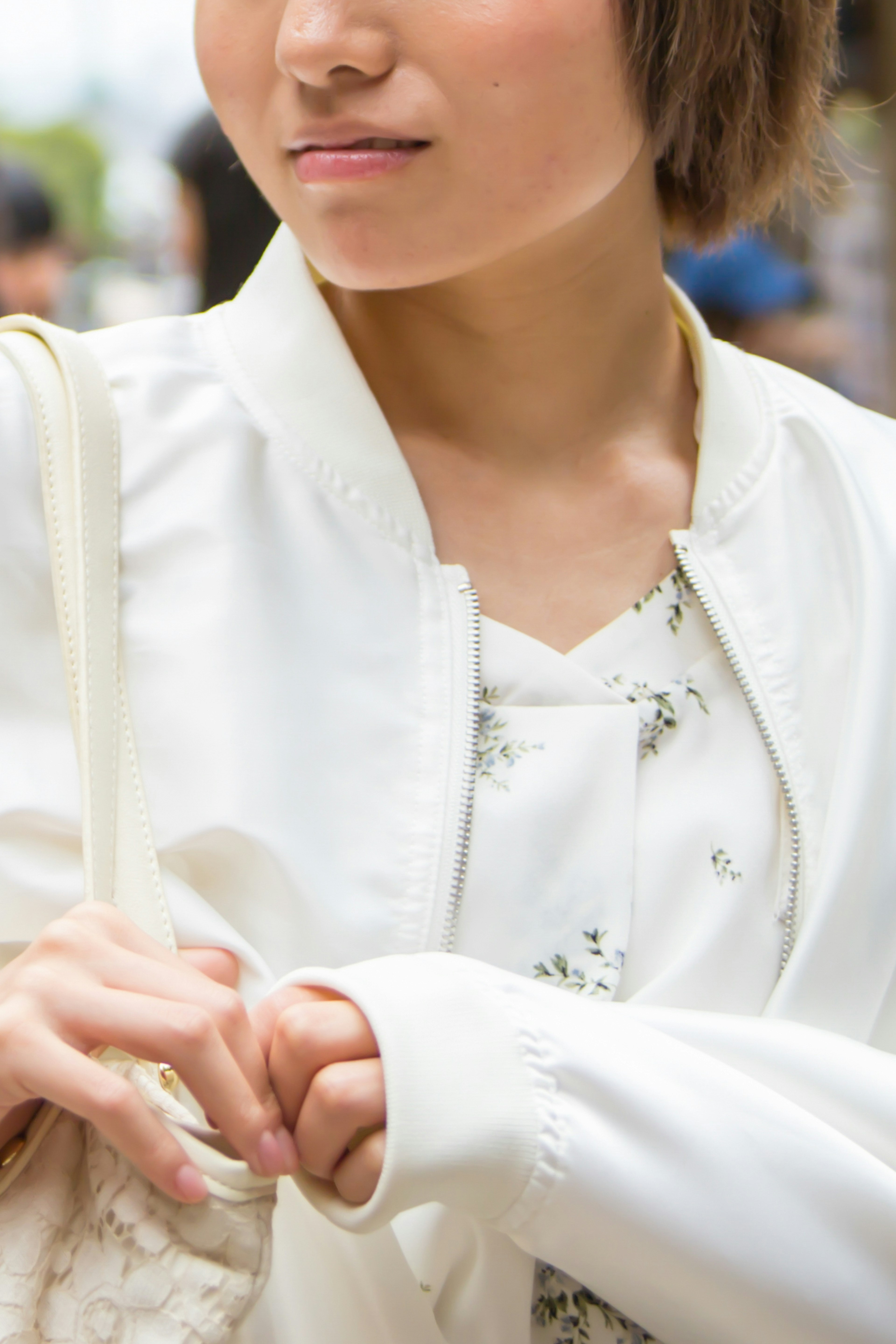 Close-up of a woman wearing a white jacket holding a bag with a subtle floral shirt underneath