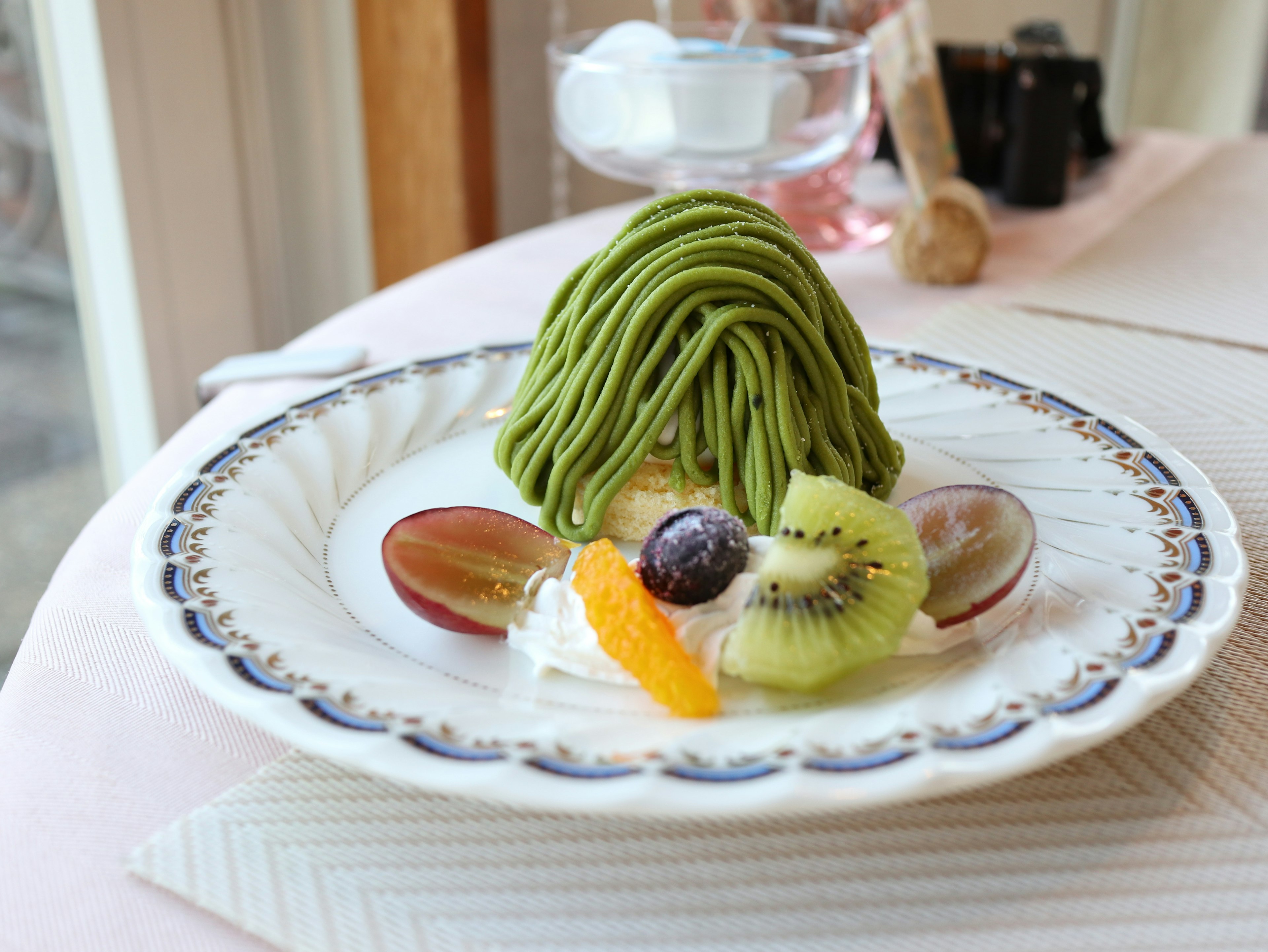 Pastel Mont Blanc de matcha bellamente presentado con frutas y crema en un plato decorativo