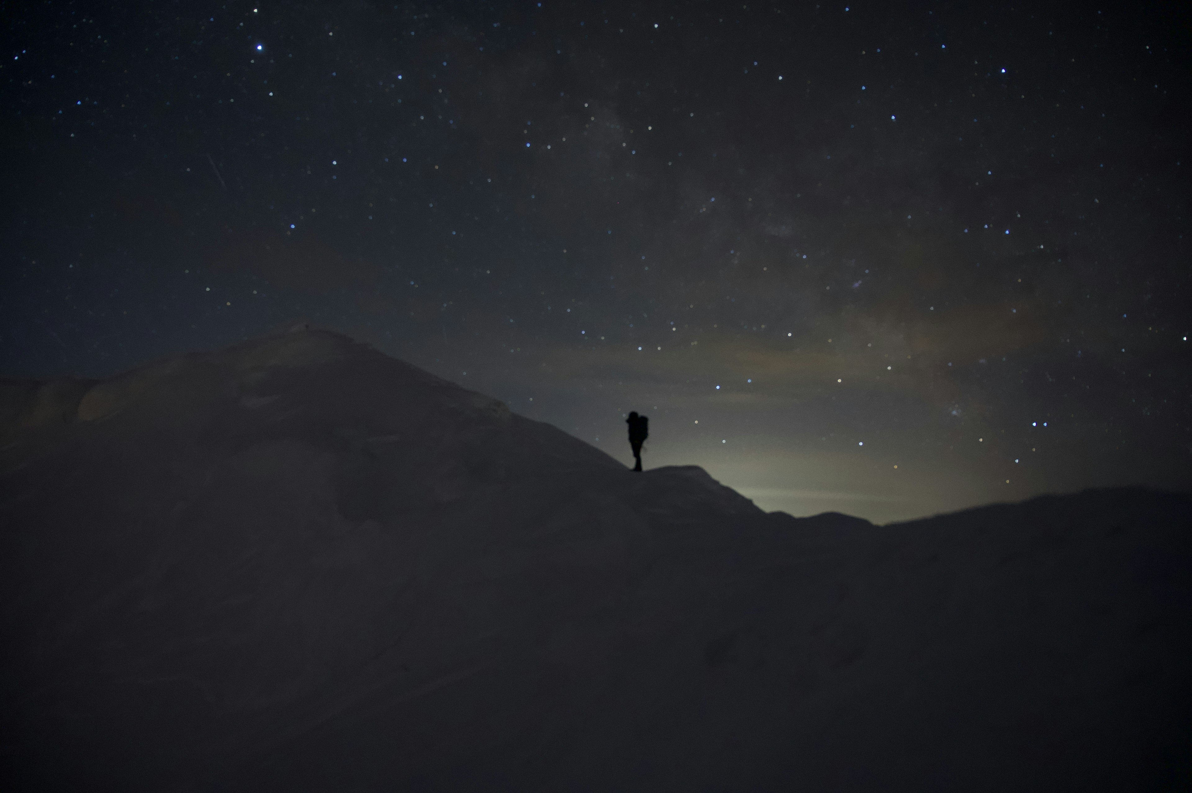 Silhouette di una persona in piedi sotto un cielo stellato con montagne innevate