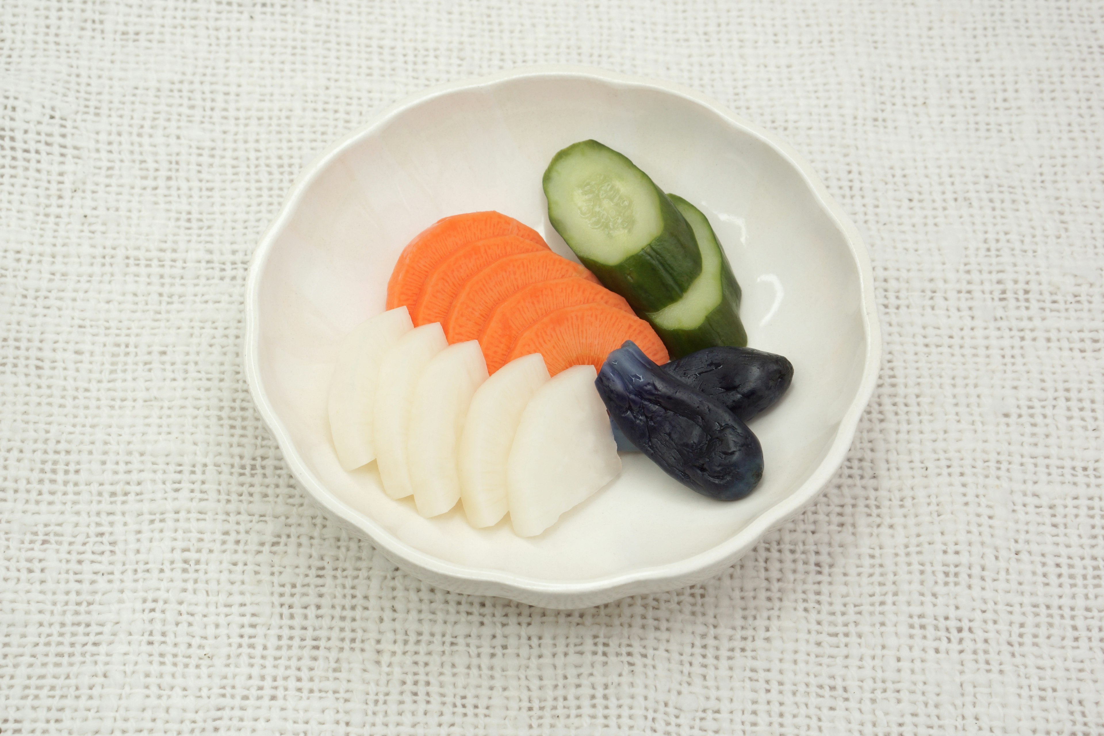 Sliced radish carrot cucumber and black fruit arranged on a white plate