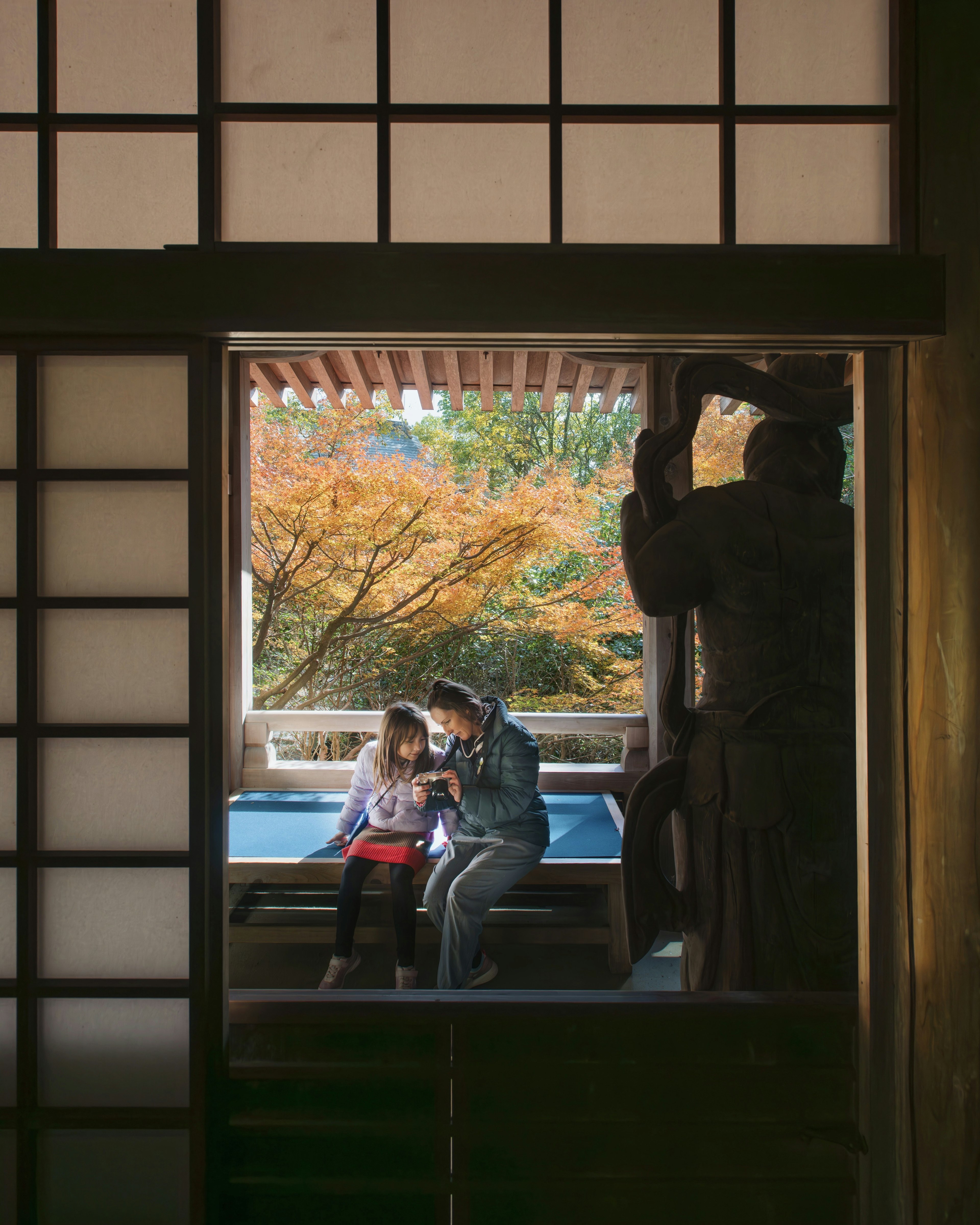 Two people sitting with an autumn landscape in the background and a sculpture