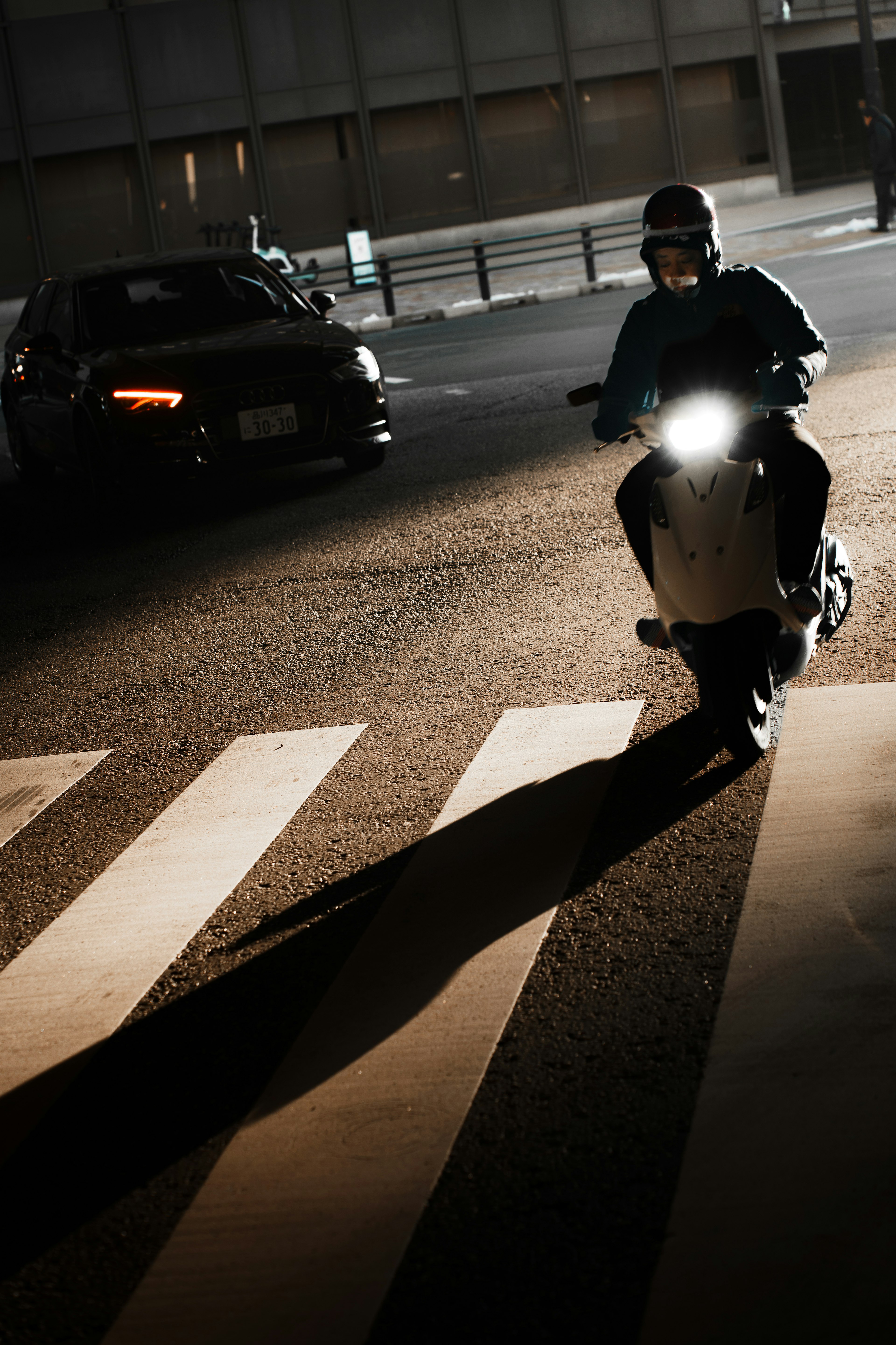 Sebuah skuter melintasi jalan di malam hari dengan bayangan yang kuat